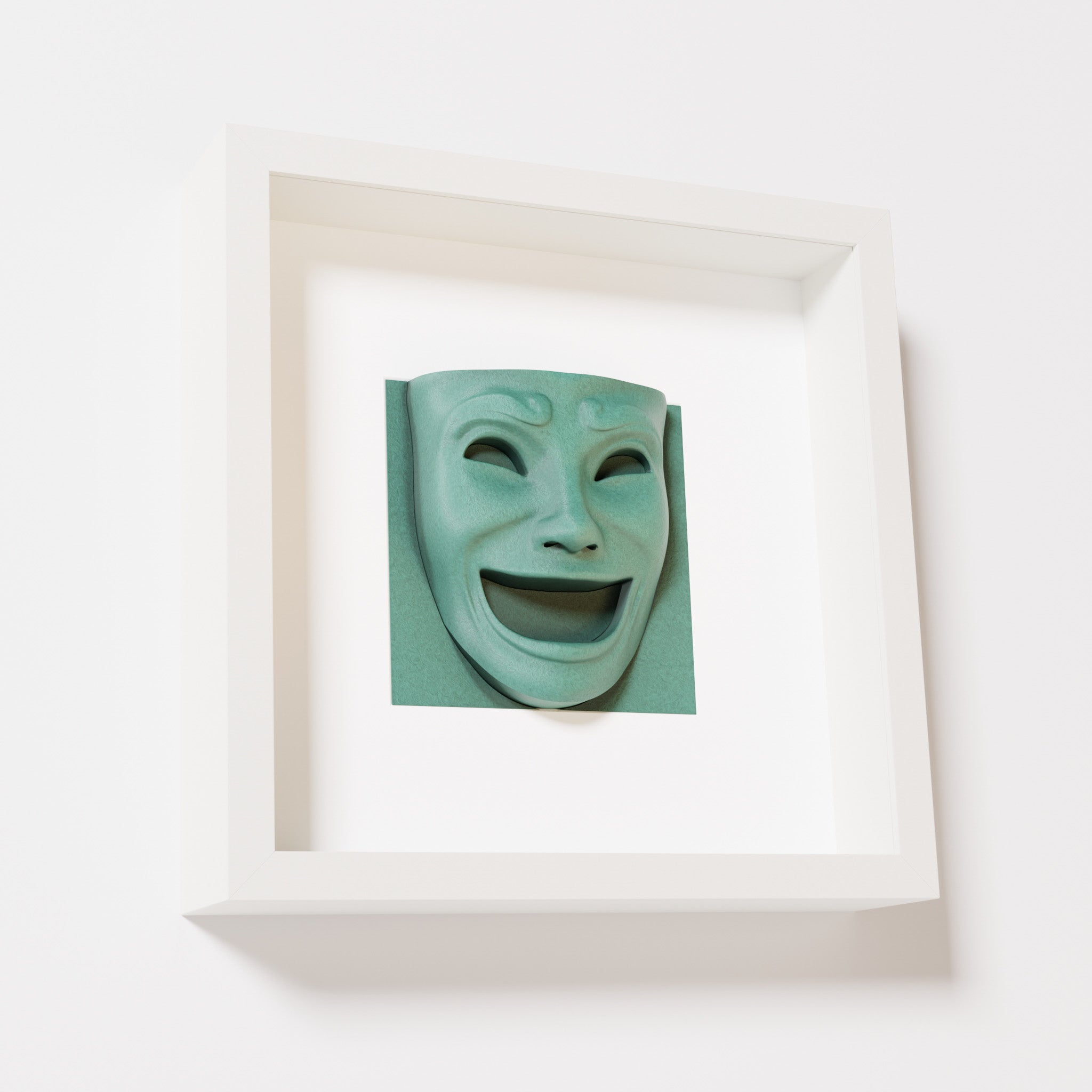 A close-up of a white shadowbox frame containing an old patina sculpture of 'Joy,' featuring a theatrical mask with a wide smile and expressive features, evoking happiness and positivity.