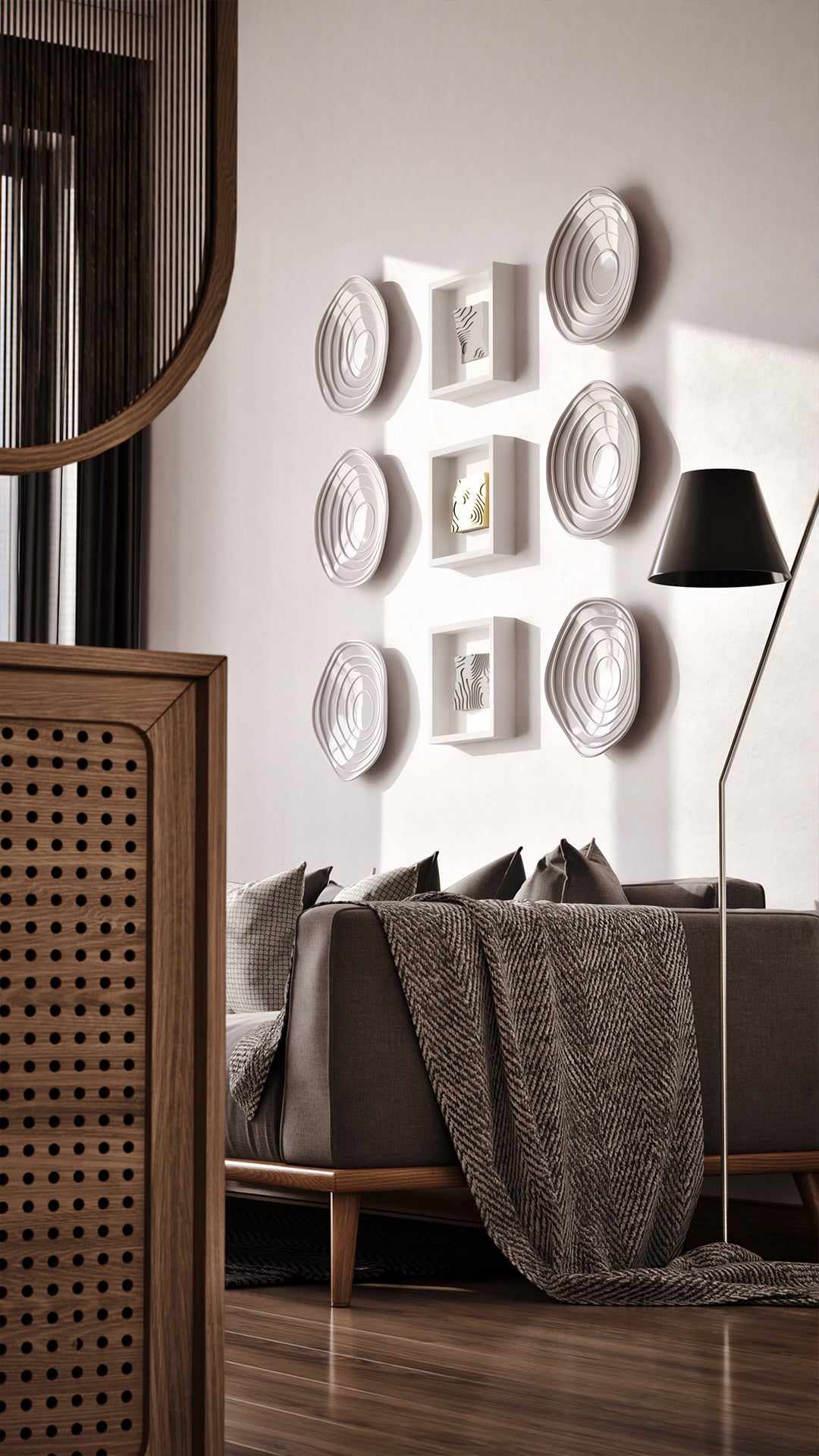 A sophisticated living area featuring a cozy gray sofa adorned with textured cushions and a herringbone throw, set against a wall showcasing a curated arrangement of layered white sculptures and illuminated shadowbox frames. The warm wood accents and soft lighting create a harmonious and inviting atmosphere, complemented by modern furniture and design elements.