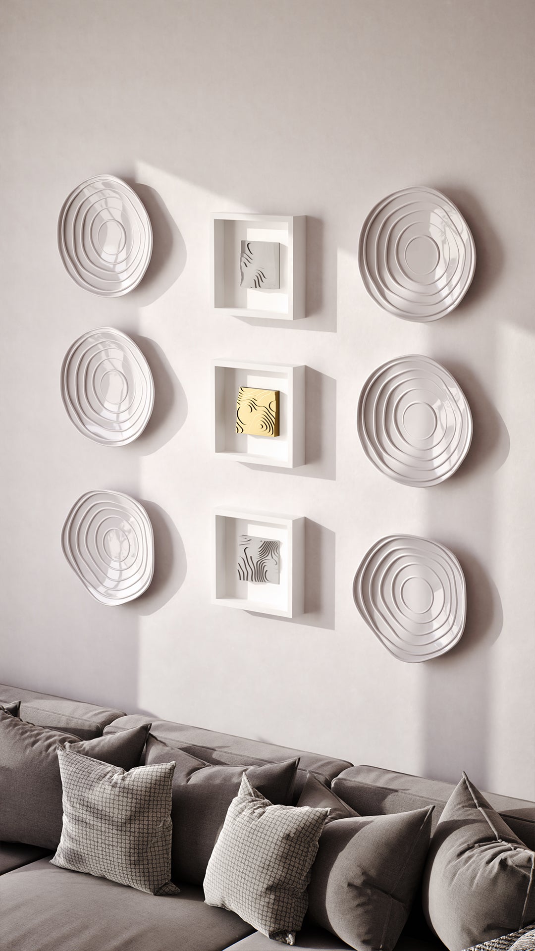 A sophisticated living area featuring a cozy gray sofa adorned with textured cushions and a herringbone throw, set against a wall showcasing a curated arrangement of layered white sculptures and illuminated shadowbox frames. The warm wood accents and soft lighting create a harmonious and inviting atmosphere, complemented by modern furniture and design elements.