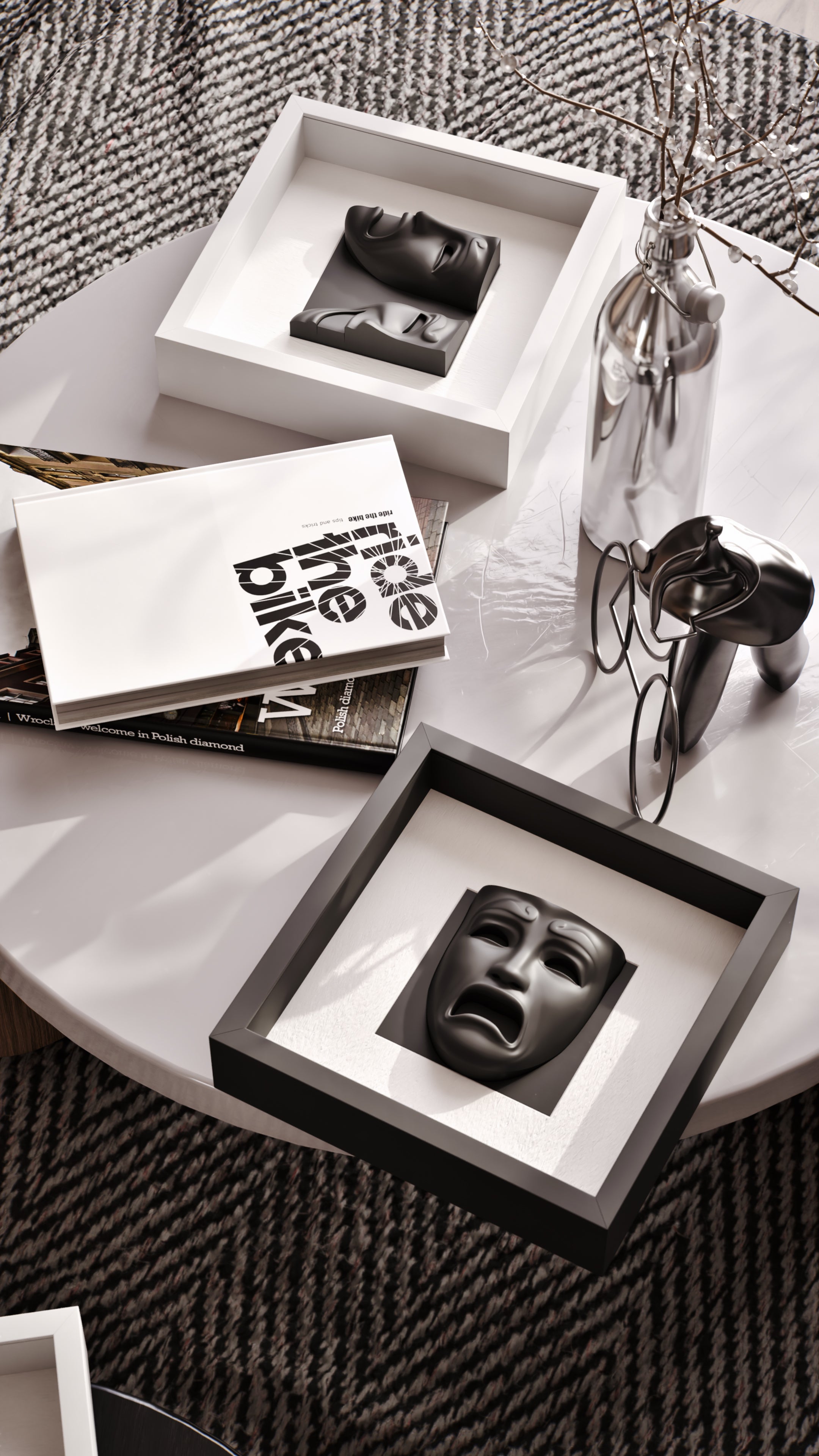 A chic coffee table arrangement featuring matte black sculptural masks encased in both white and black shadowbox frames. Complemented by a curated selection of books, a polished silver vase, and modern decor, the setup exudes sophistication and artistic flair against the textured herringbone rug.