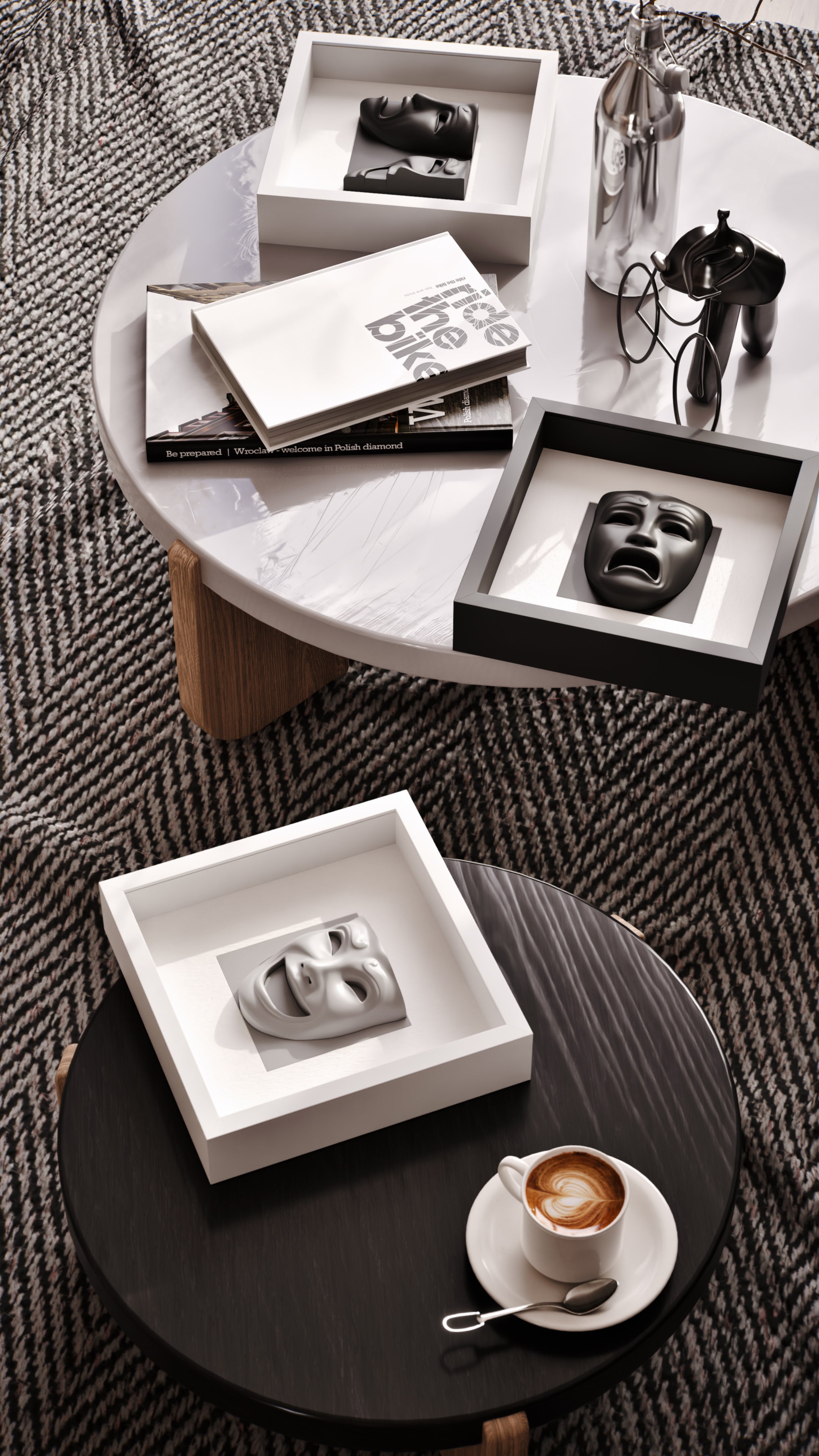 A chic coffee table arrangement featuring matte black sculptural masks encased in both white and black shadowbox frames. Complemented by a curated selection of books, a polished silver vase, and modern decor, the setup exudes sophistication and artistic flair against the textured herringbone rug.