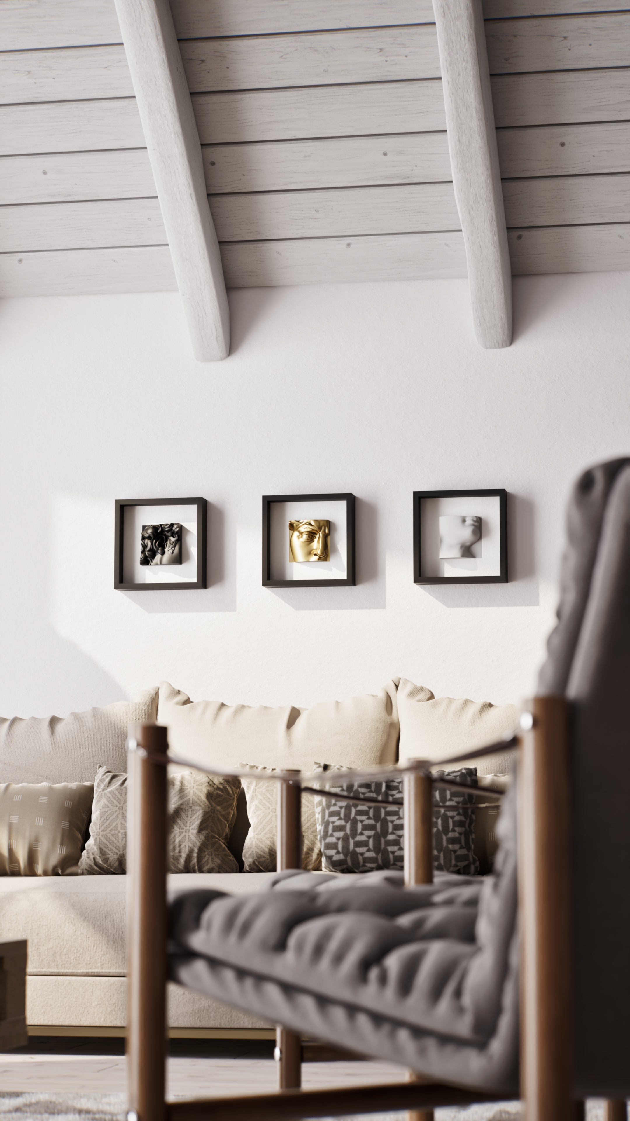 A cozy living room setup with a light beige sofa adorned with patterned cushions, set against a white wall featuring three black shadowbox frames displaying elegant sculptures in black, gold, and white. The space is complemented by a wooden table in the foreground and exposed beam ceilings, creating a warm and inviting atmosphere.