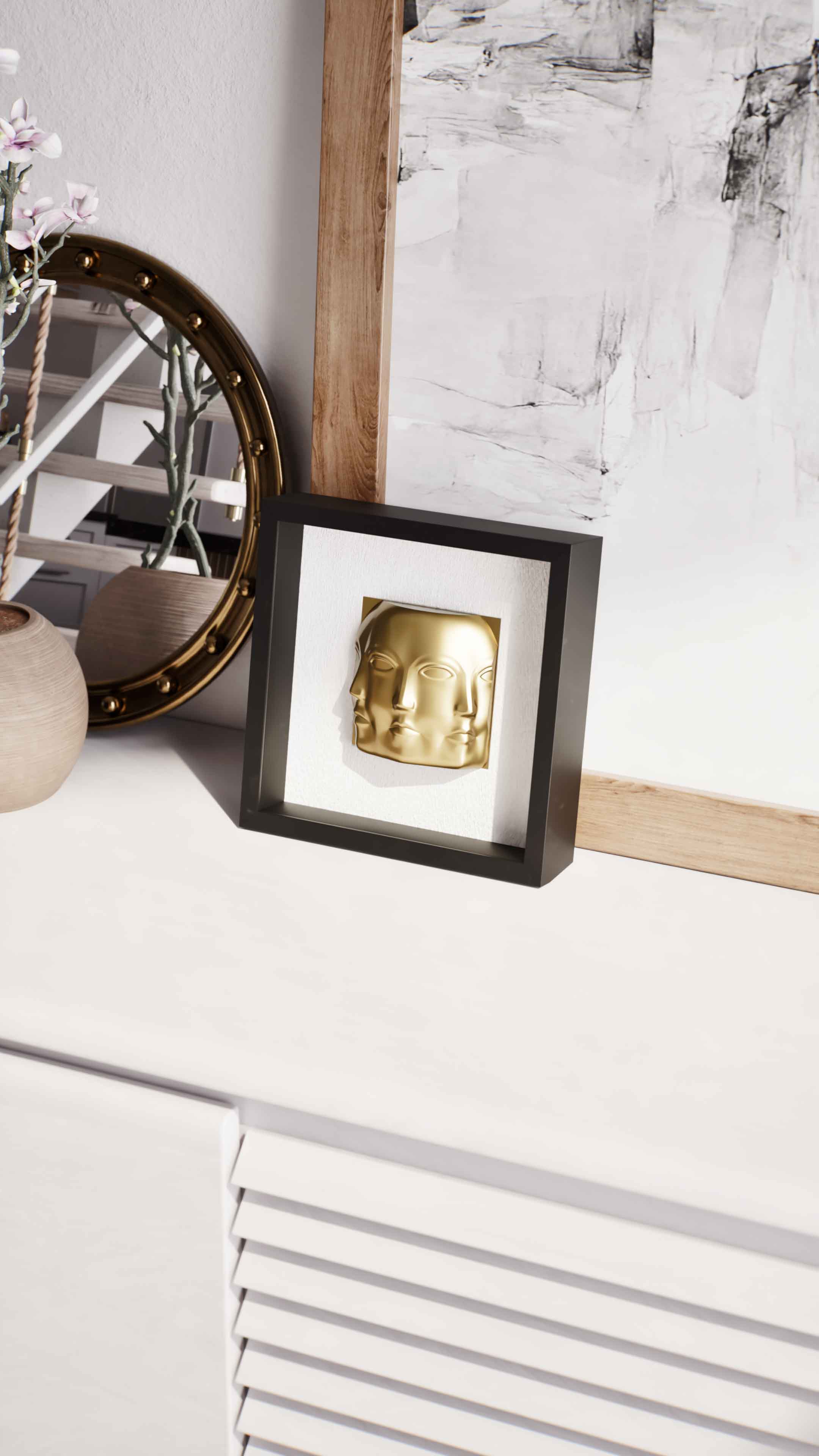 A close-up of a black shadowbox frame featuring a gold three-faced sculpture, displayed on a sleek white cabinet. The setting is complemented by a round, gold-rimmed mirror and a textured wooden picture frame in the background, adding layers of elegance and contemporary style to the composition.