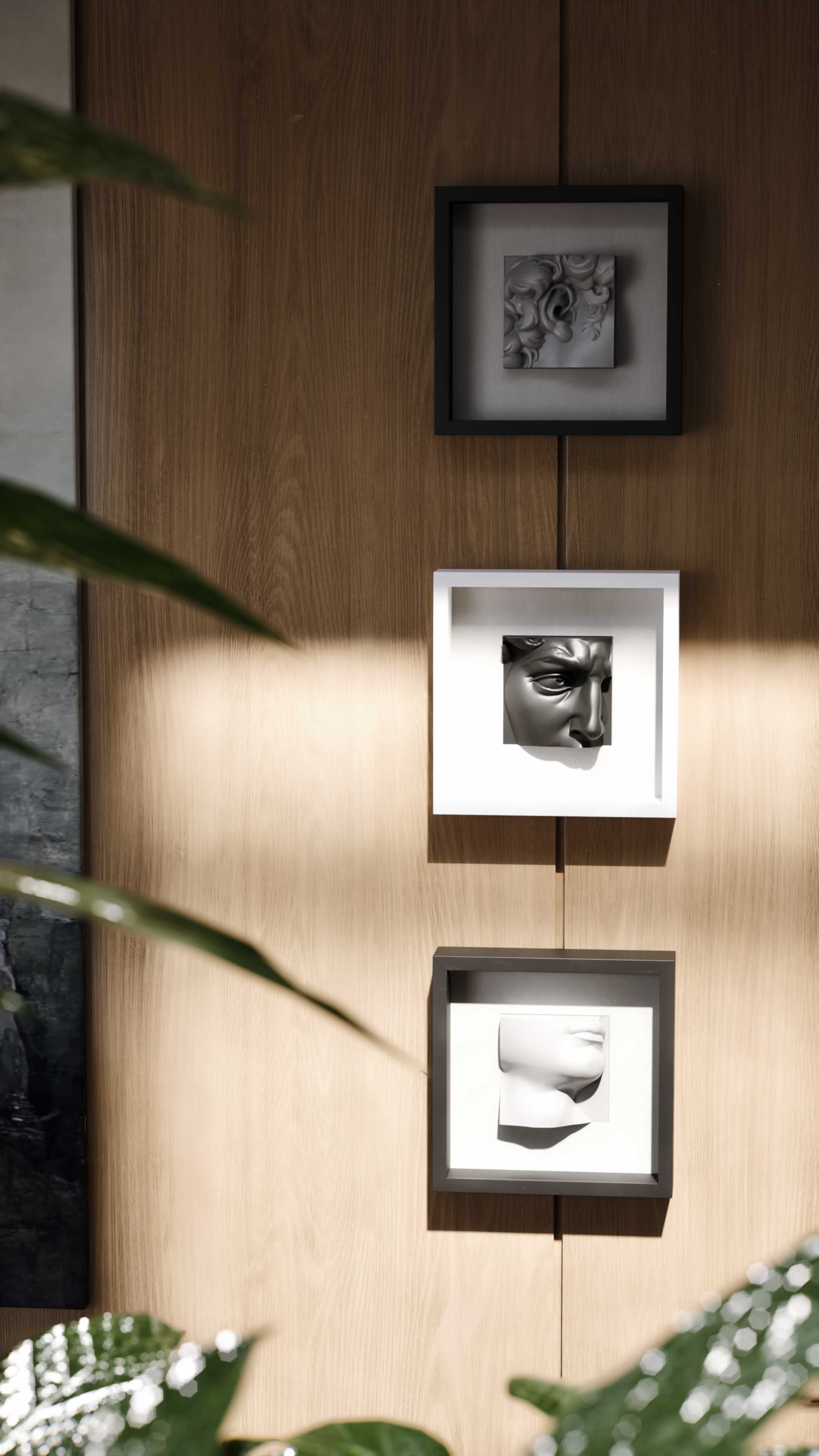 Three shadowbox frames arranged vertically on a wooden wall, featuring sculptural artwork. The top frame, in black, encloses a white detailed floral sculpture. The middle white frame holds a black profile sculpture of a human face, and the bottom black frame displays a minimalist white sculpture of a human bust. Adjacent is an abstract painting, adding depth and artistic harmony to the space.