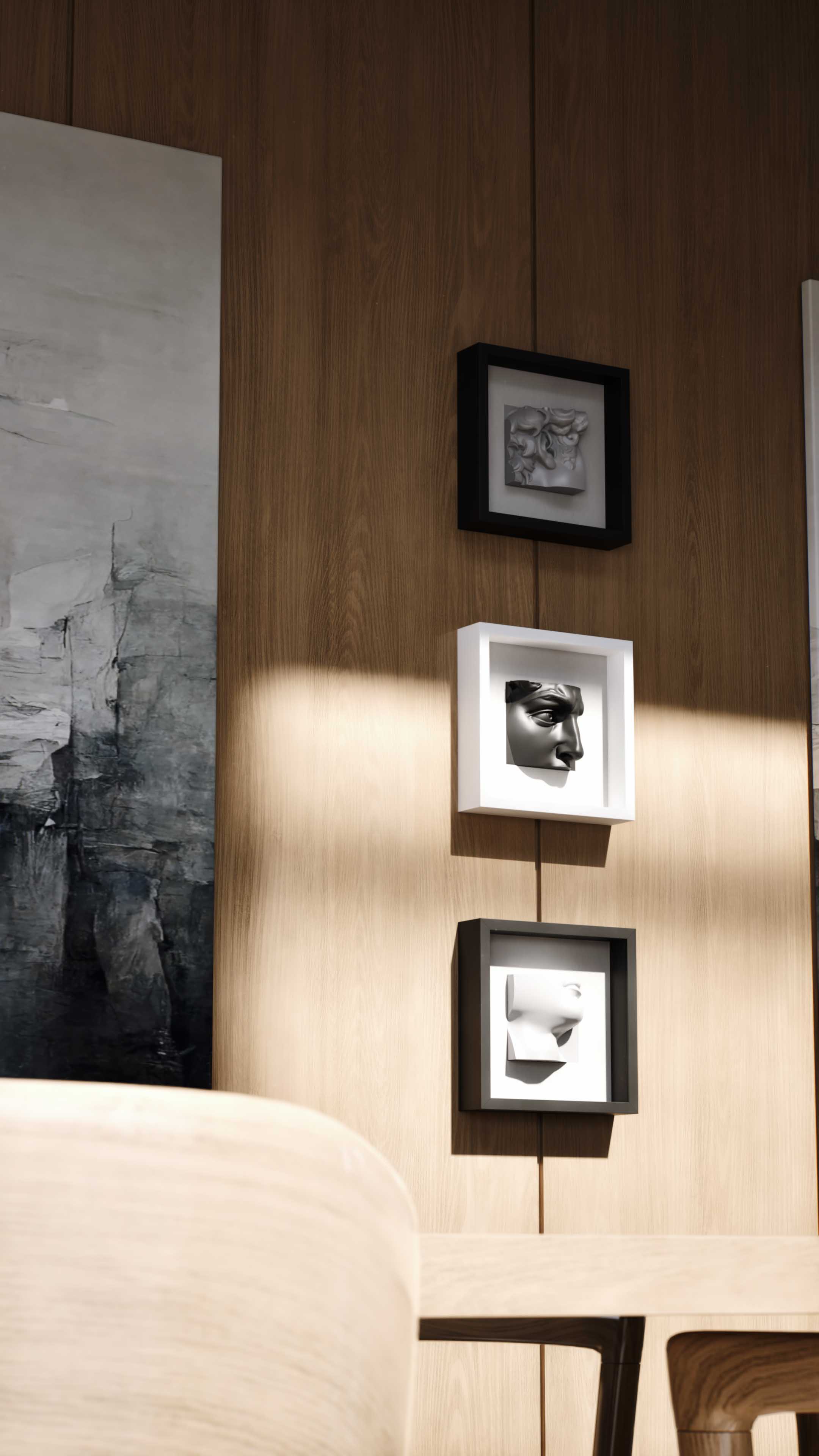 Three shadowbox frames arranged vertically on a wooden wall, featuring sculptural artwork. The top frame, in black, encloses a white detailed floral sculpture. The middle white frame holds a black profile sculpture of a human face, and the bottom black frame displays a minimalist white sculpture of a human bust. Adjacent is an abstract painting, adding depth and artistic harmony to the space.