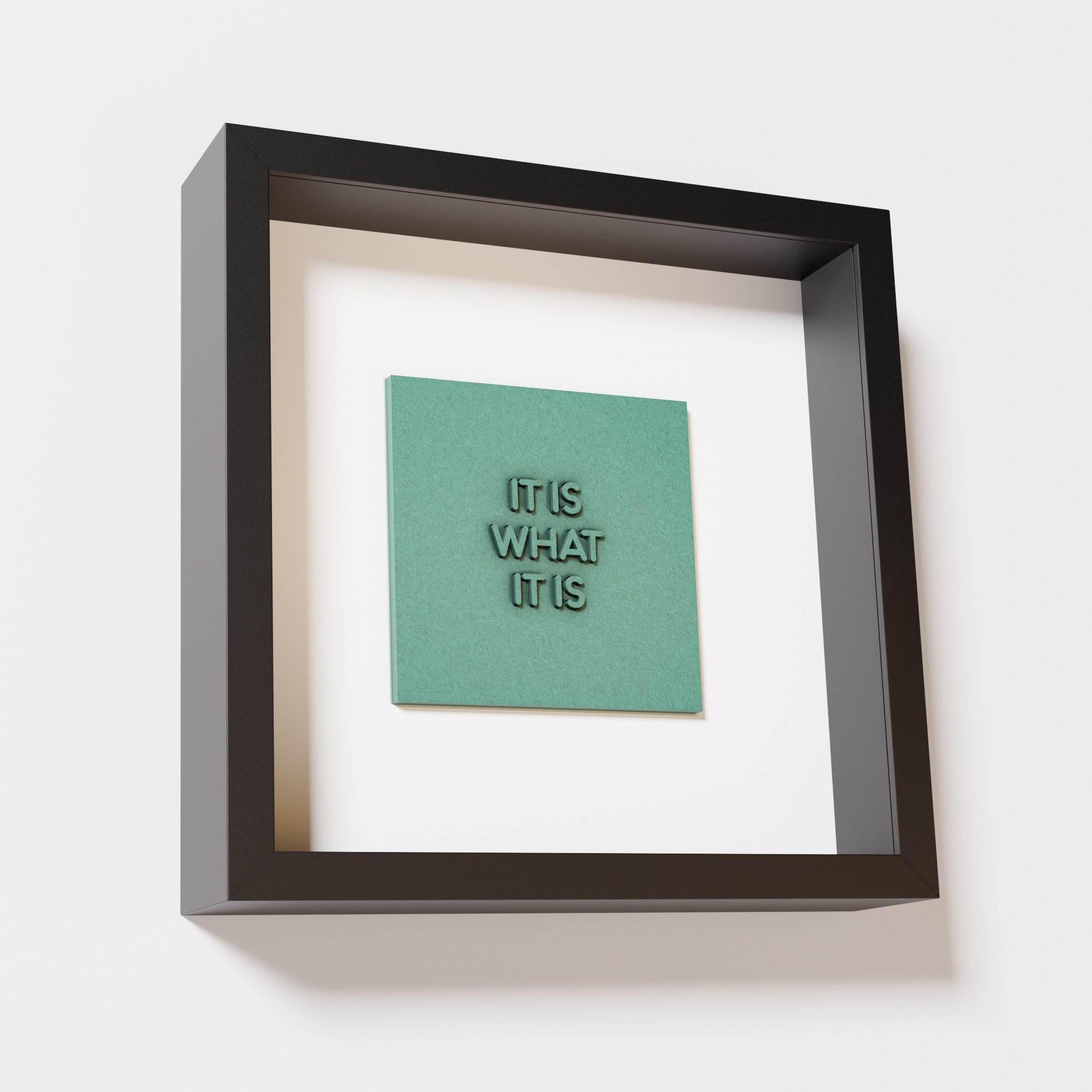 A close-up of a black shadowbox frame containing an old patina artwork featuring the bold phrase 'It Is What It Is' from 'The Chill Pill,' showcasing a textured green finish and intricate lettering.