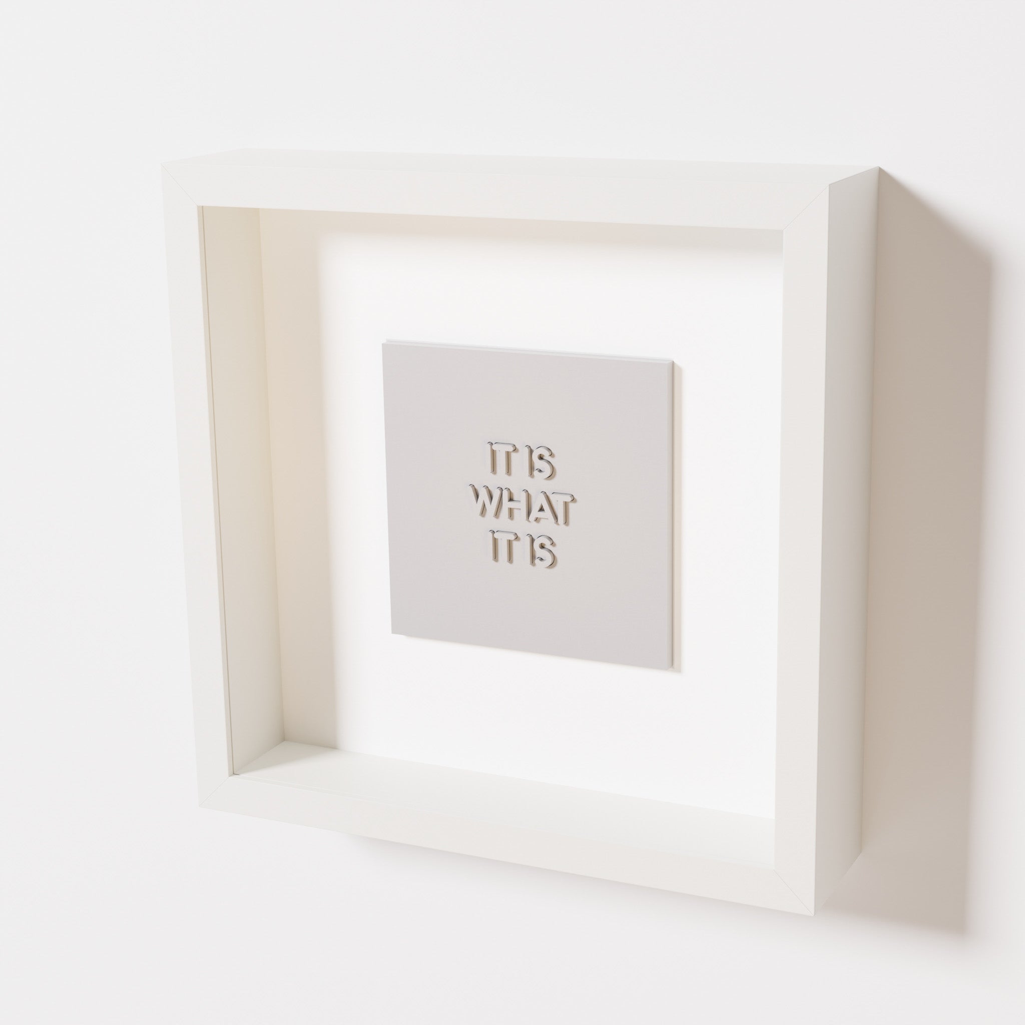 A close-up of a white shadowbox frame containing a marble white artwork featuring the bold phrase 'It Is What It Is' from 'The Chill Pill,' emphasizing its smooth lettering and refined design.
