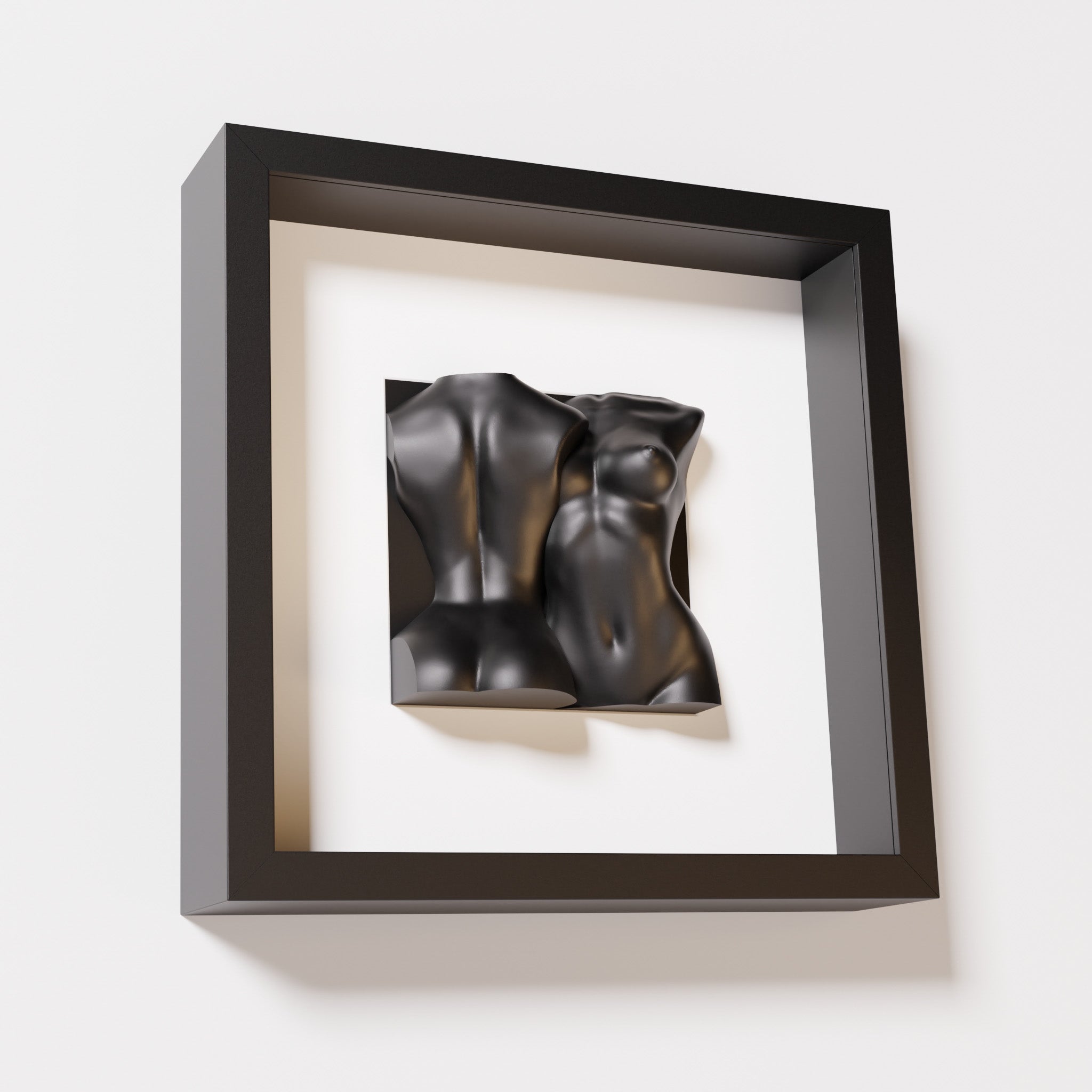 A close-up of a black shadowbox frame holding a matte black sculpture of two intertwined female bodies. The monochromatic pairing enhances the sculpture’s modern, fluid aesthetic.