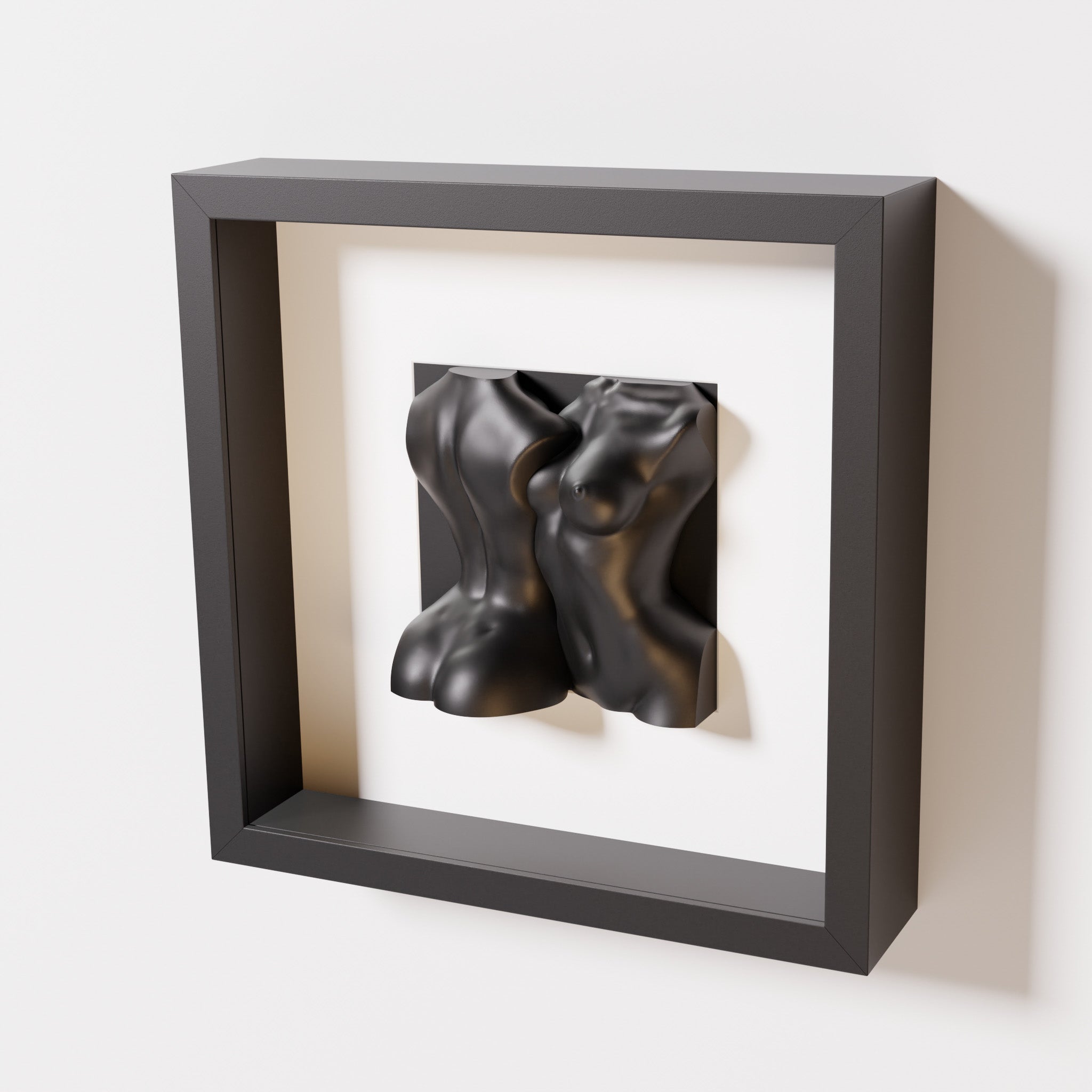 A close-up of a black shadowbox frame holding a matte black sculpture of two intertwined female bodies. The monochromatic pairing enhances the sculpture’s modern, fluid aesthetic.