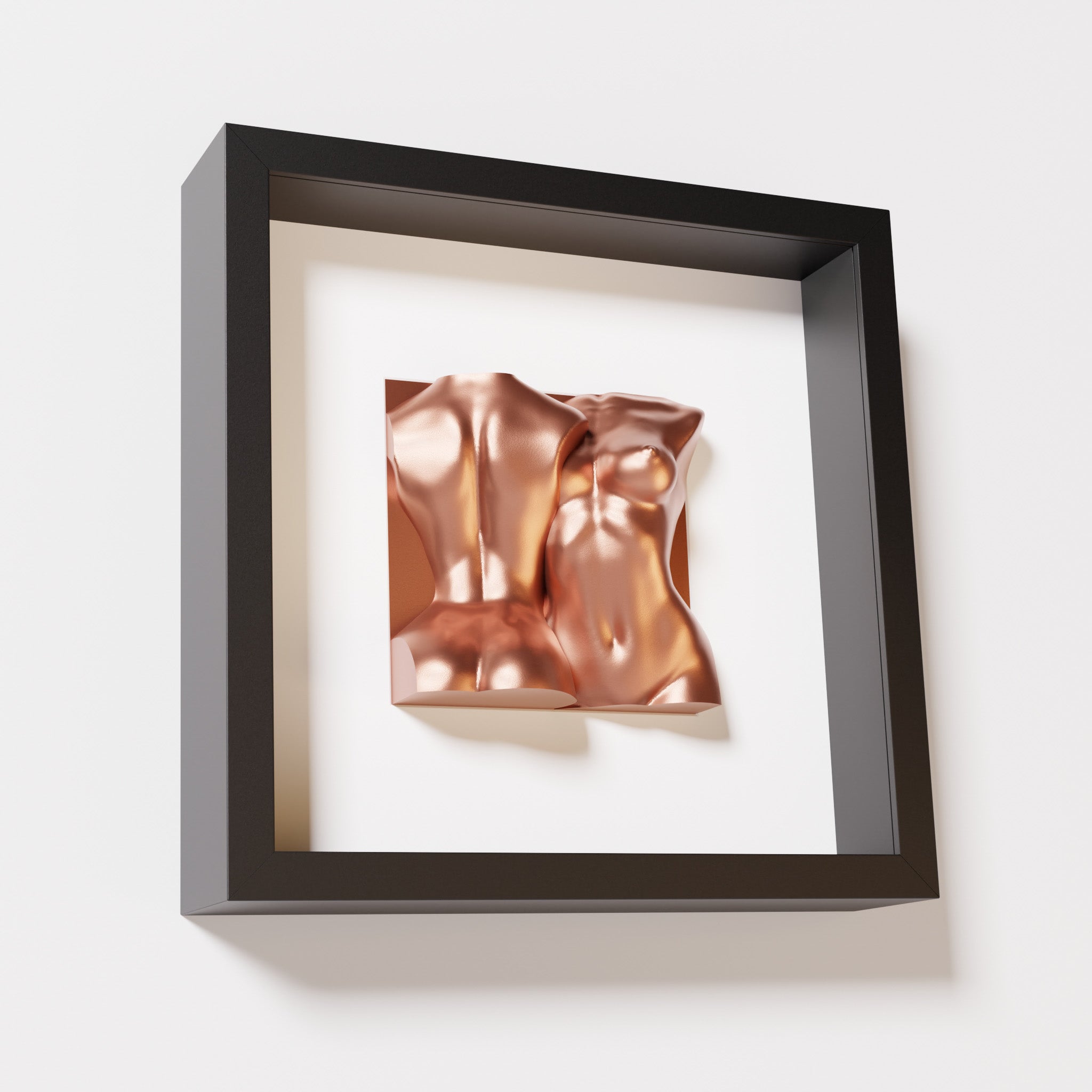 A close-up of a black shadowbox frame containing a chrome copper sculpture of two intertwined female bodies. The reflective copper tones contrast beautifully with the dark frame for a sophisticated look.