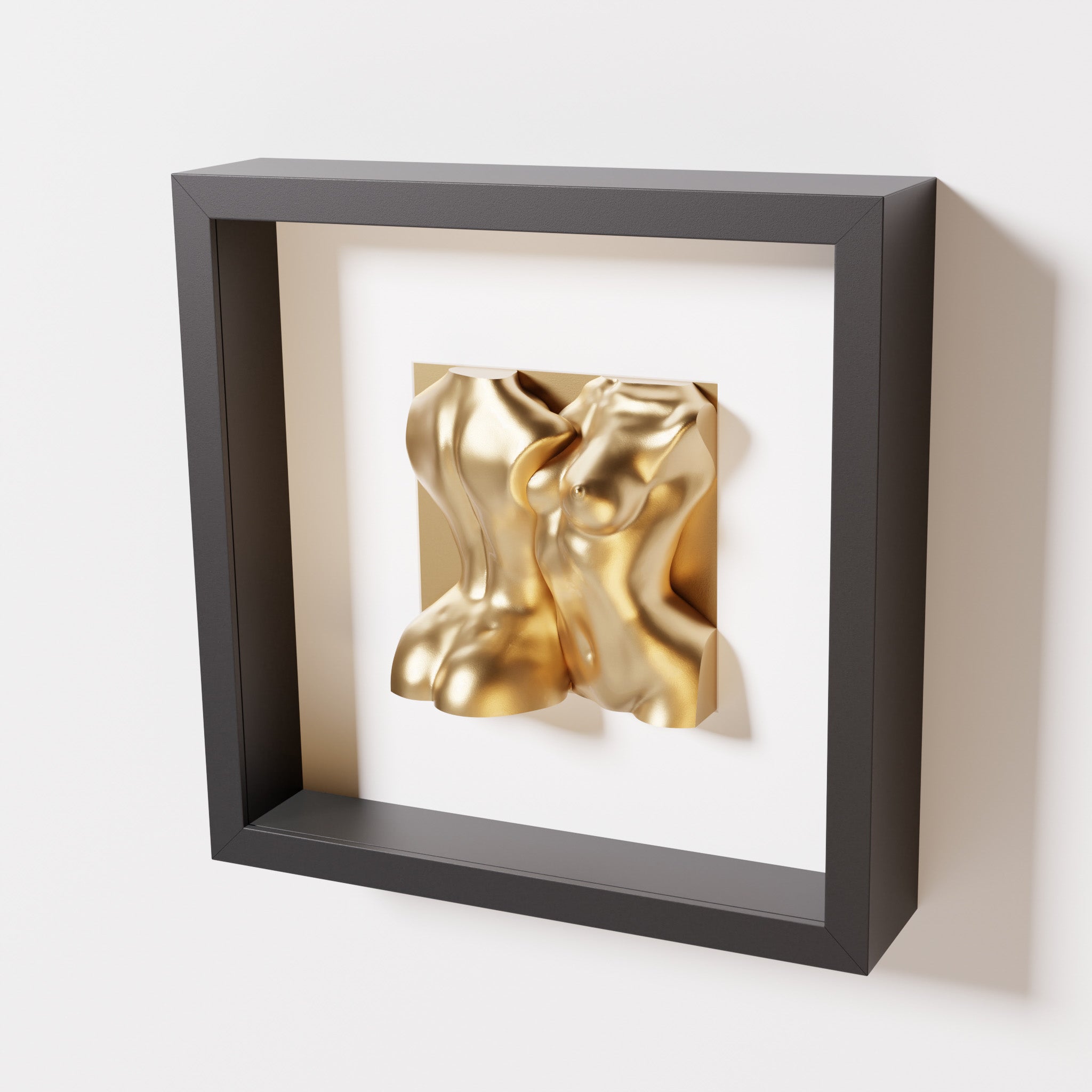 A close-up of a black shadowbox frame holding a chrome gold sculpture of two intertwined female bodies. The reflective gold finish stands out boldly against the sleek black frame for a luxurious effect.