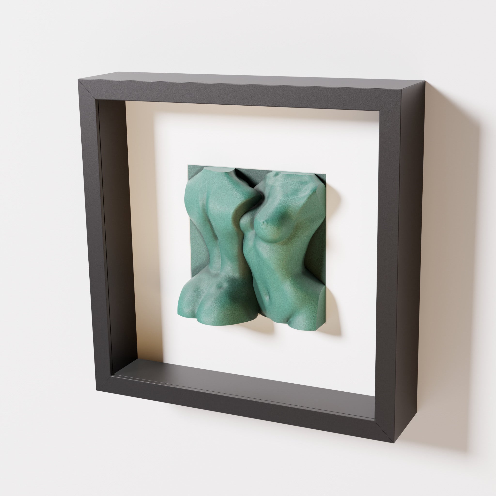 A close-up of a black shadowbox frame containing an old patina sculpture of two intertwined female bodies. The weathered green texture contrasts beautifully with the sleek black frame.