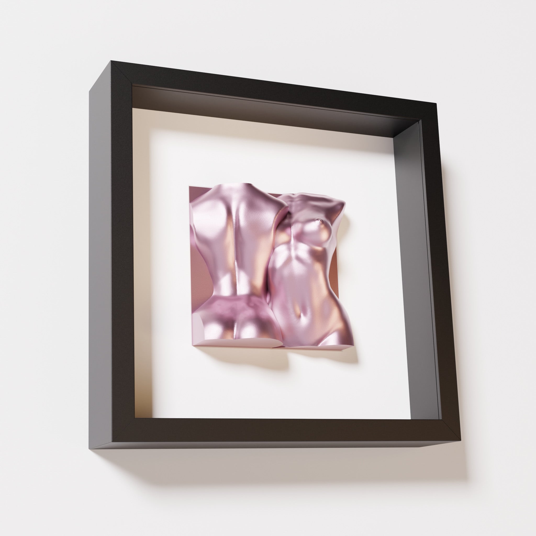 A close-up of a black shadowbox frame containing a metallic rose sculpture of two intertwined female bodies. The reflective pink finish contrasts beautifully with the sleek black frame for a bold, modern look.