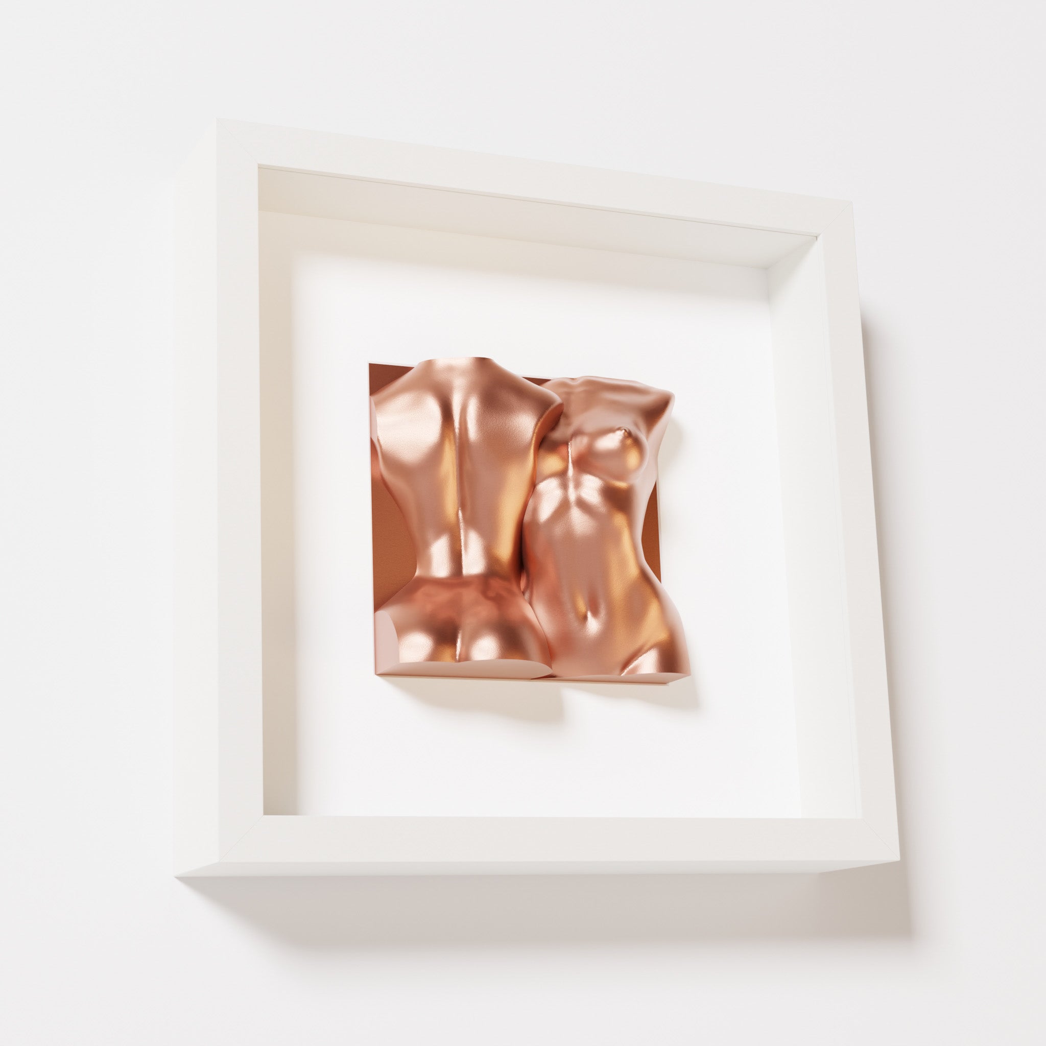 A close-up of a white shadowbox frame containing a chrome copper sculpture of two intertwined female bodies. The warm metallic tones and fluid forms create a contemporary and inviting aesthetic.