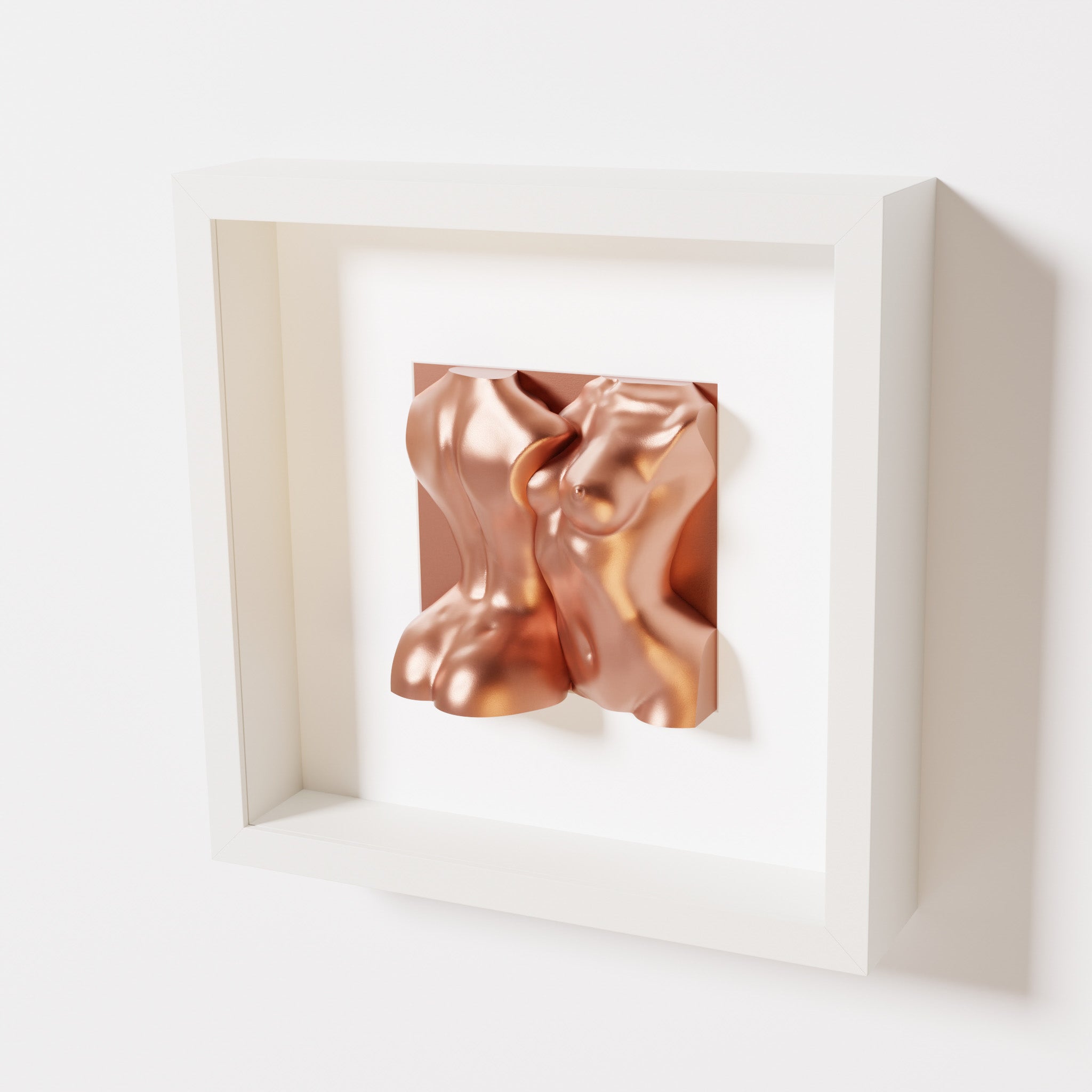 A close-up of a white shadowbox frame containing a chrome copper sculpture of two intertwined female bodies. The warm metallic tones and fluid forms create a contemporary and inviting aesthetic.