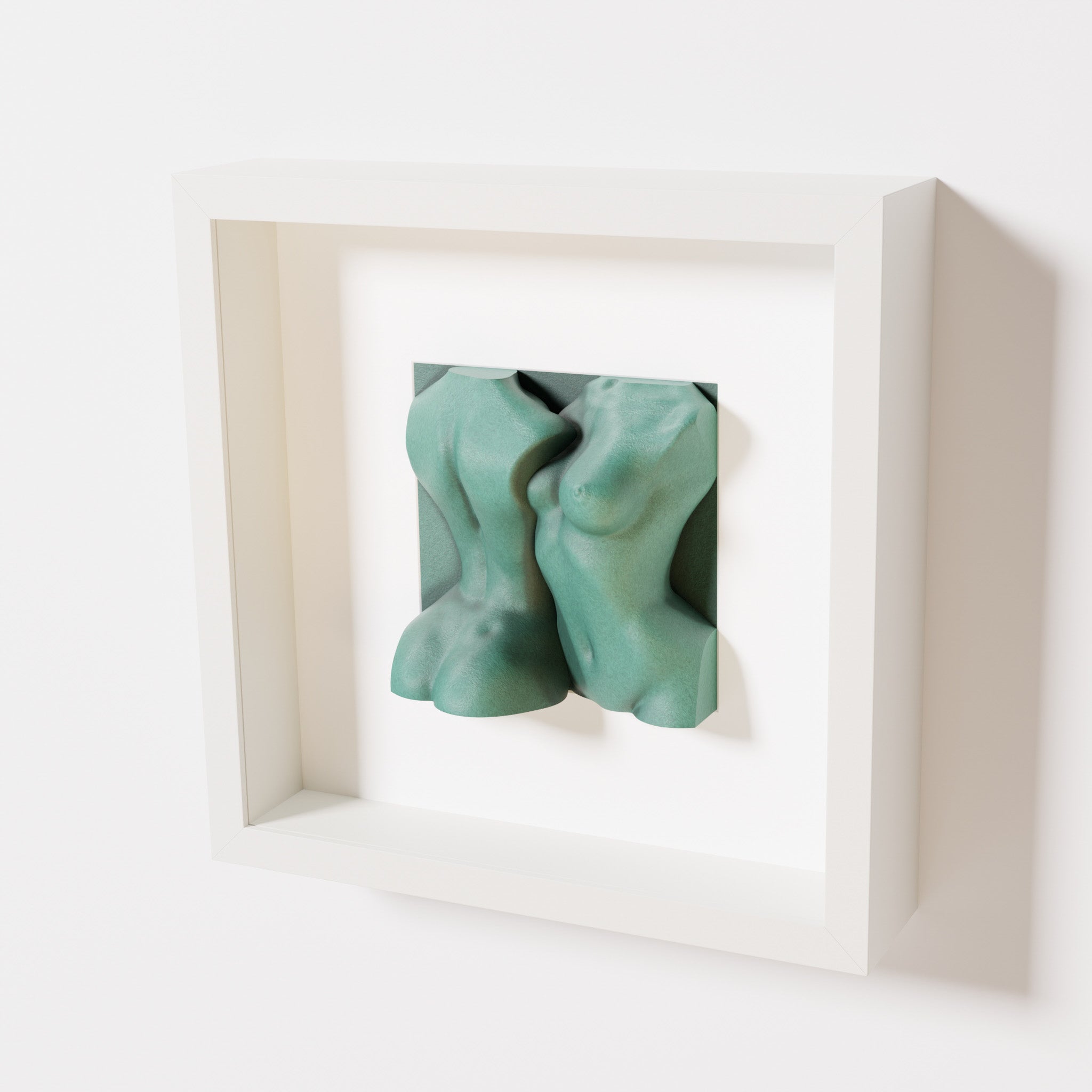 A close-up of a white shadowbox frame containing an old patina sculpture of two intertwined female bodies. The textured, weathered green finish lends a classical and timeless character to the artwork.