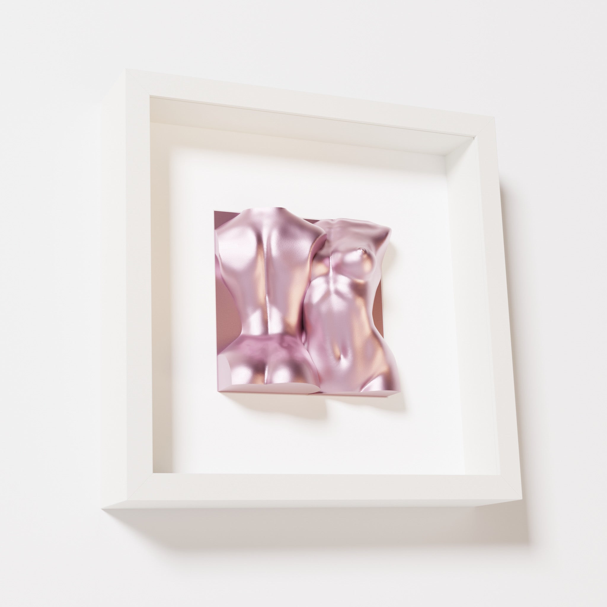 A close-up of a white shadowbox frame holding a metallic rose sculpture of two intertwined female bodies. The soft pink metallic finish enhances the fluid, contemporary forms with a feminine touch.