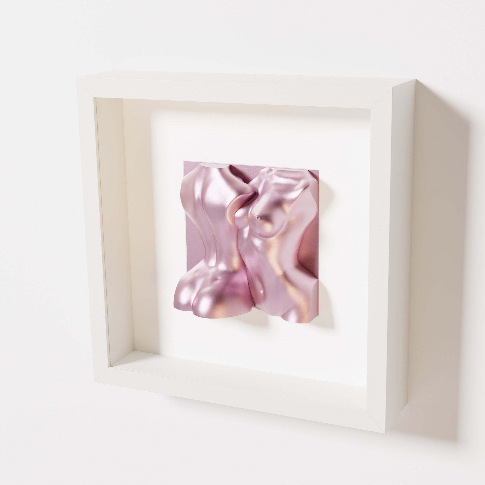 A close-up of a white shadowbox frame holding a metallic rose sculpture of two intertwined female bodies. The soft pink metallic finish enhances the fluid, contemporary forms with a feminine touch.