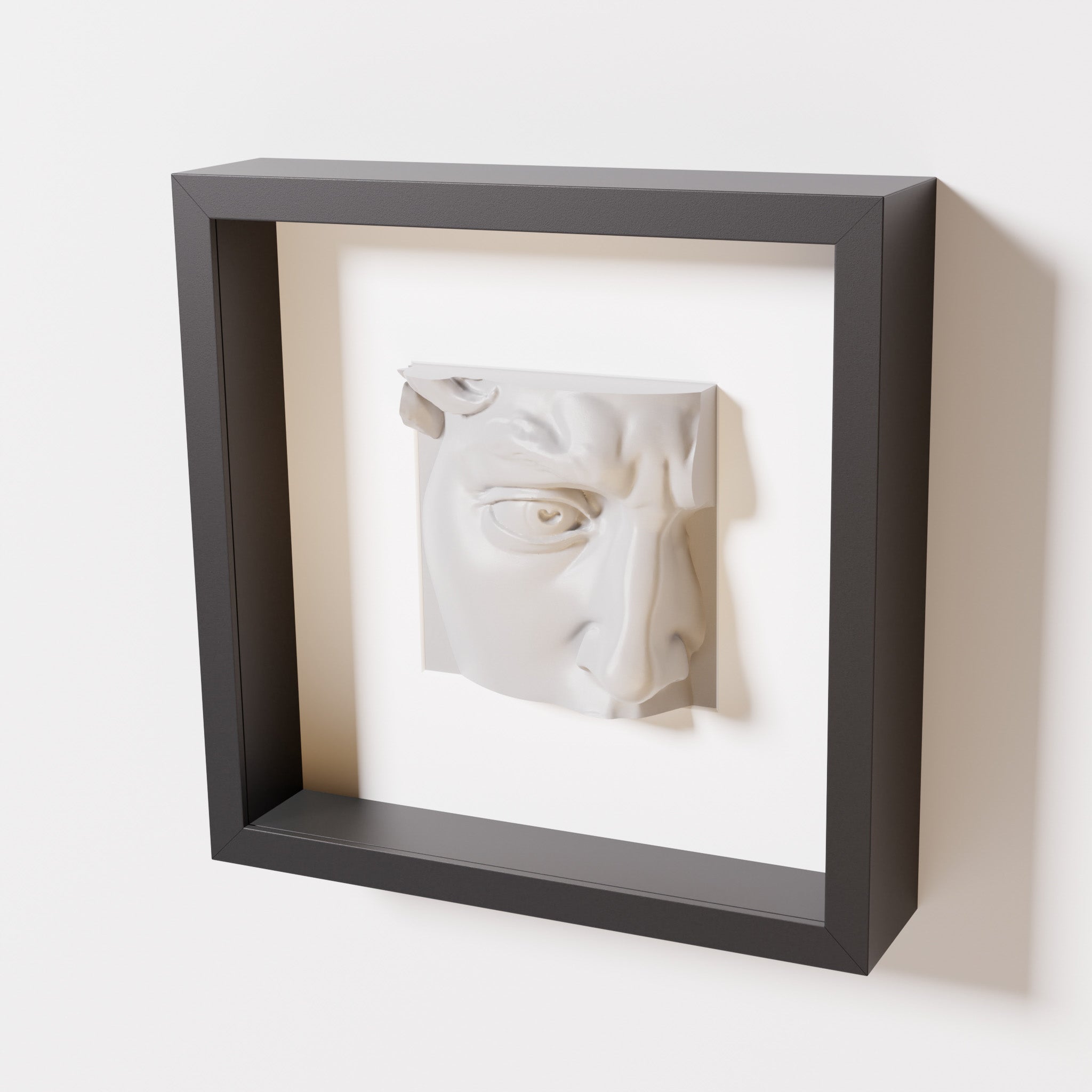 A close-up of a black shadowbox frame containing a marble white sculpture of 'David's Eye,' highlighting the intricate details of the eye, brow, and surrounding textures.