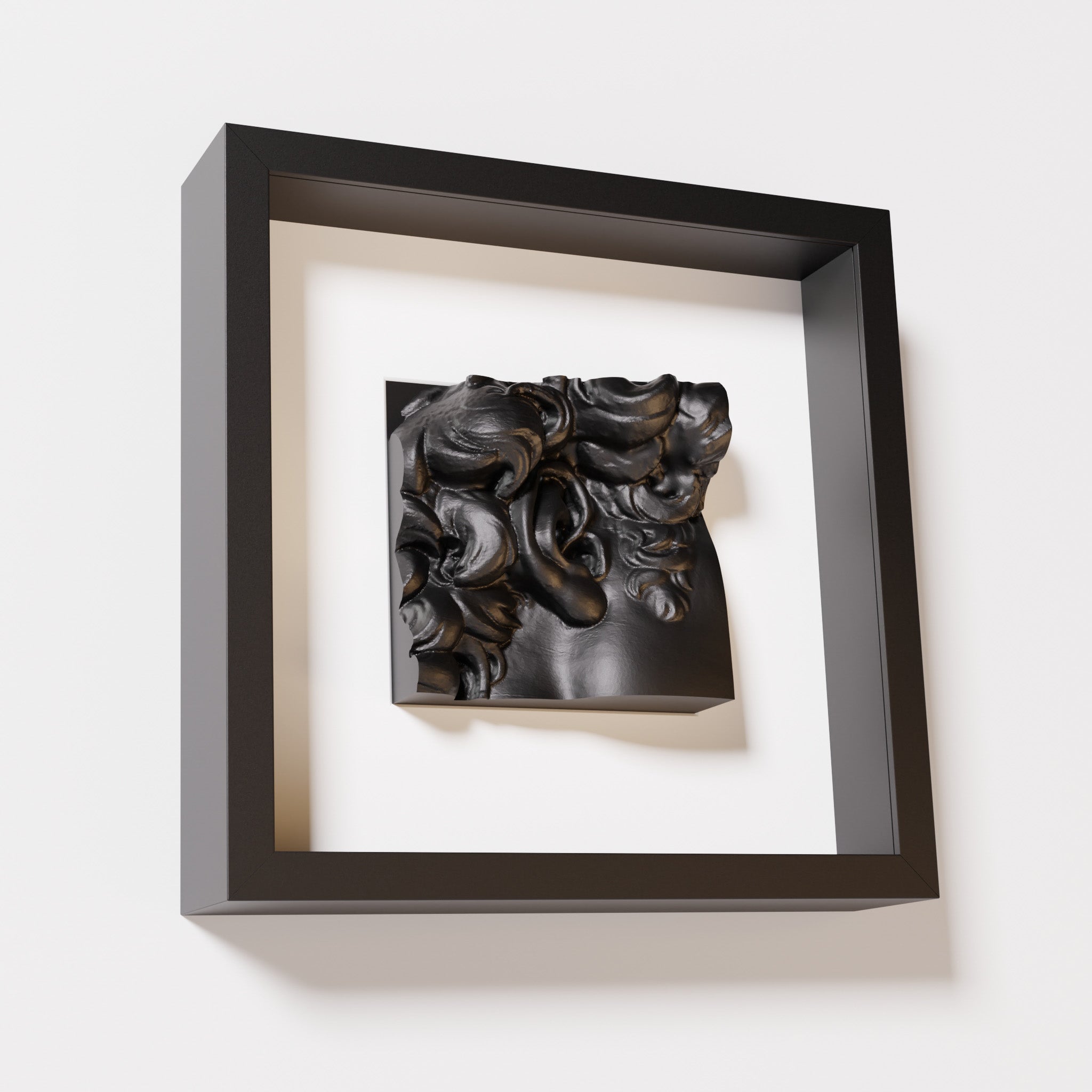 A close-up of a black shadowbox frame containing a matte black sculpture of 'David's Ear.' The detailed curls and ear stand out against the sleek black frame.