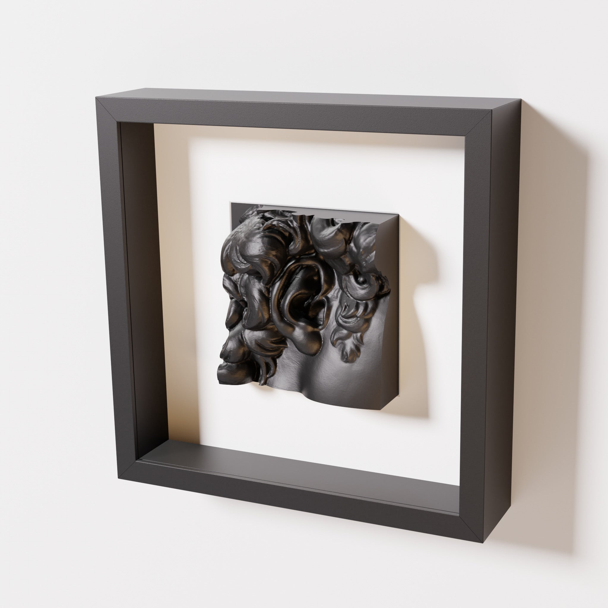 A close-up of a black shadowbox frame containing a matte black sculpture of 'David's Ear.' The detailed curls and ear stand out against the sleek black frame.