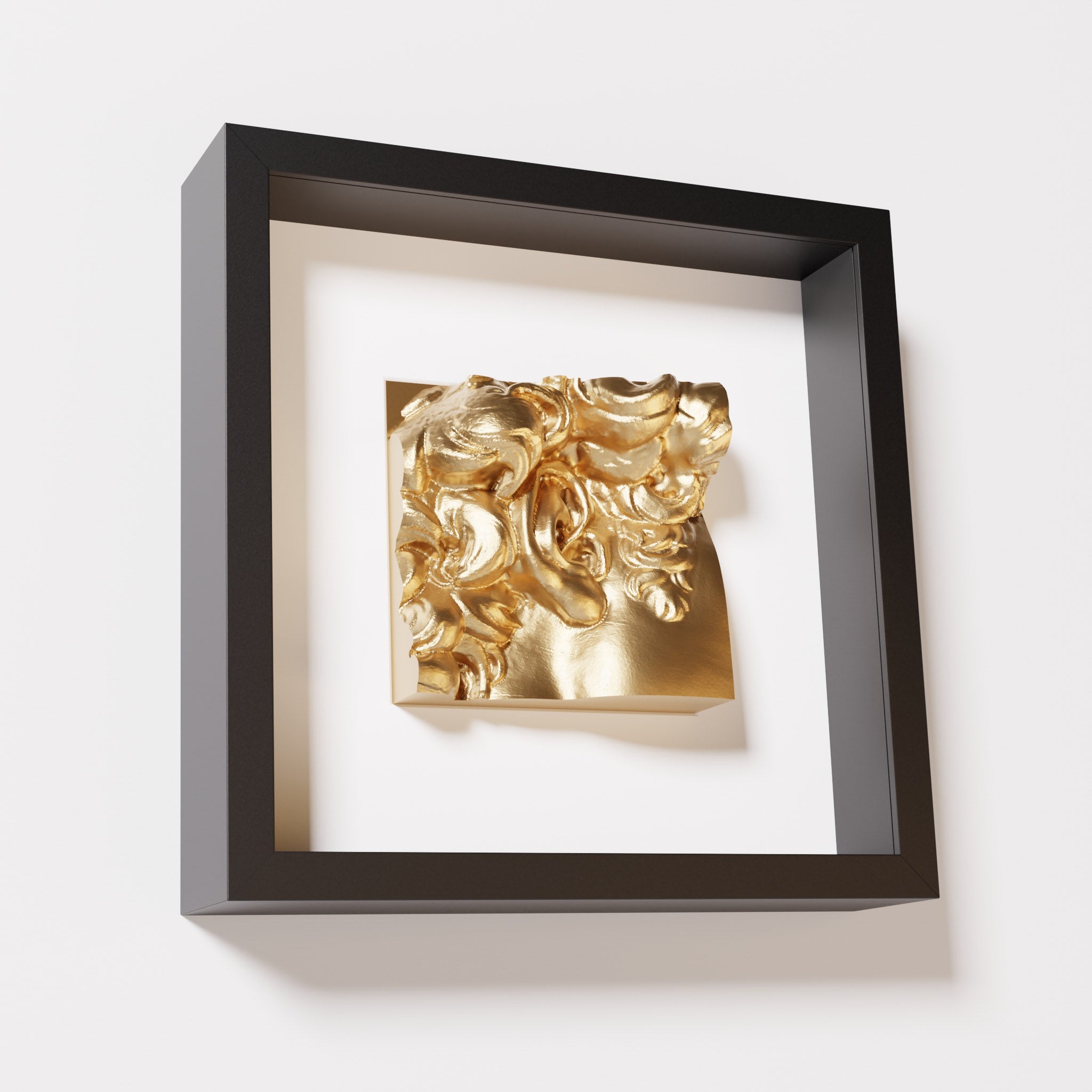 A close-up of a black shadowbox frame featuring a chrome gold sculpture of 'David's Ear.' The shiny gold finish and intricate ear details stand out against the black frame.