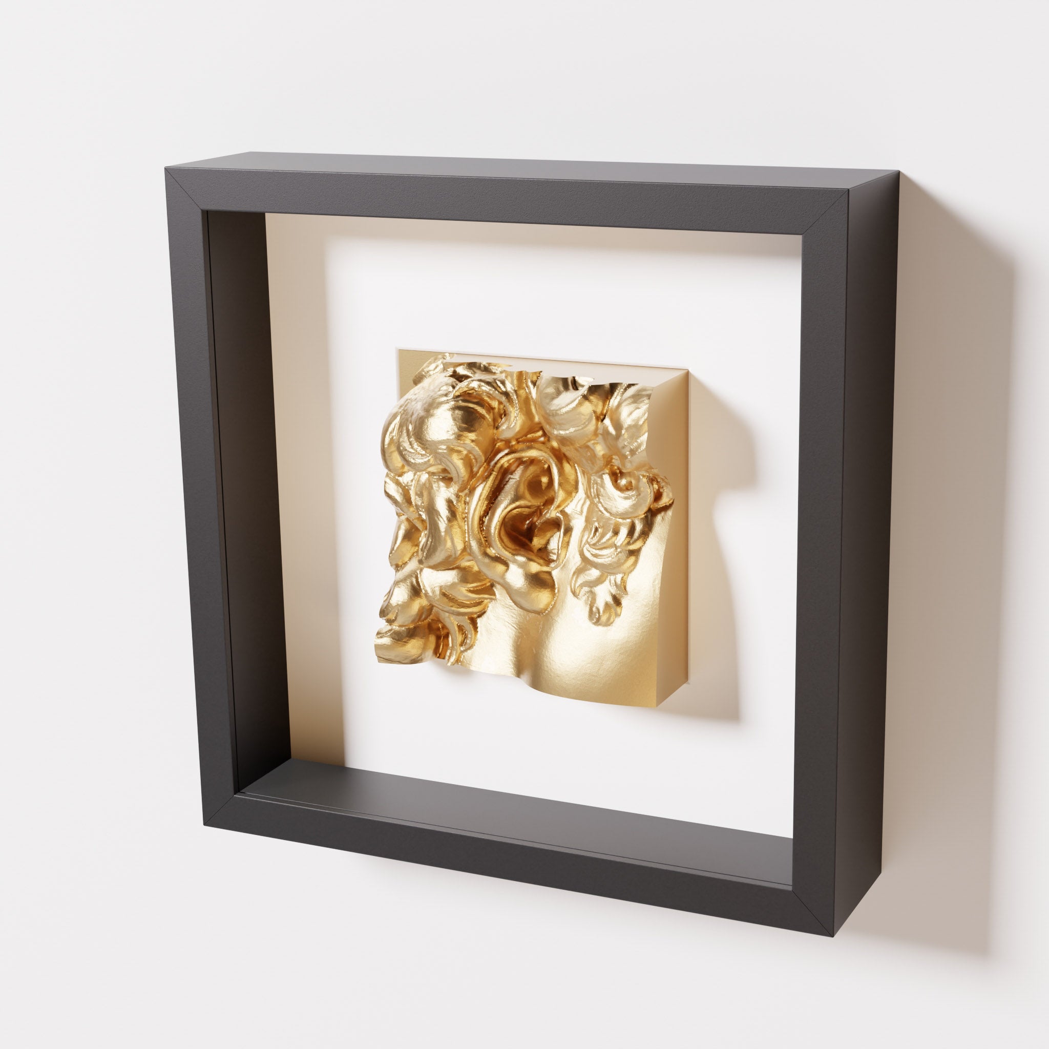 A close-up of a black shadowbox frame featuring a chrome gold sculpture of 'David's Ear.' The shiny gold finish and intricate ear details stand out against the black frame.