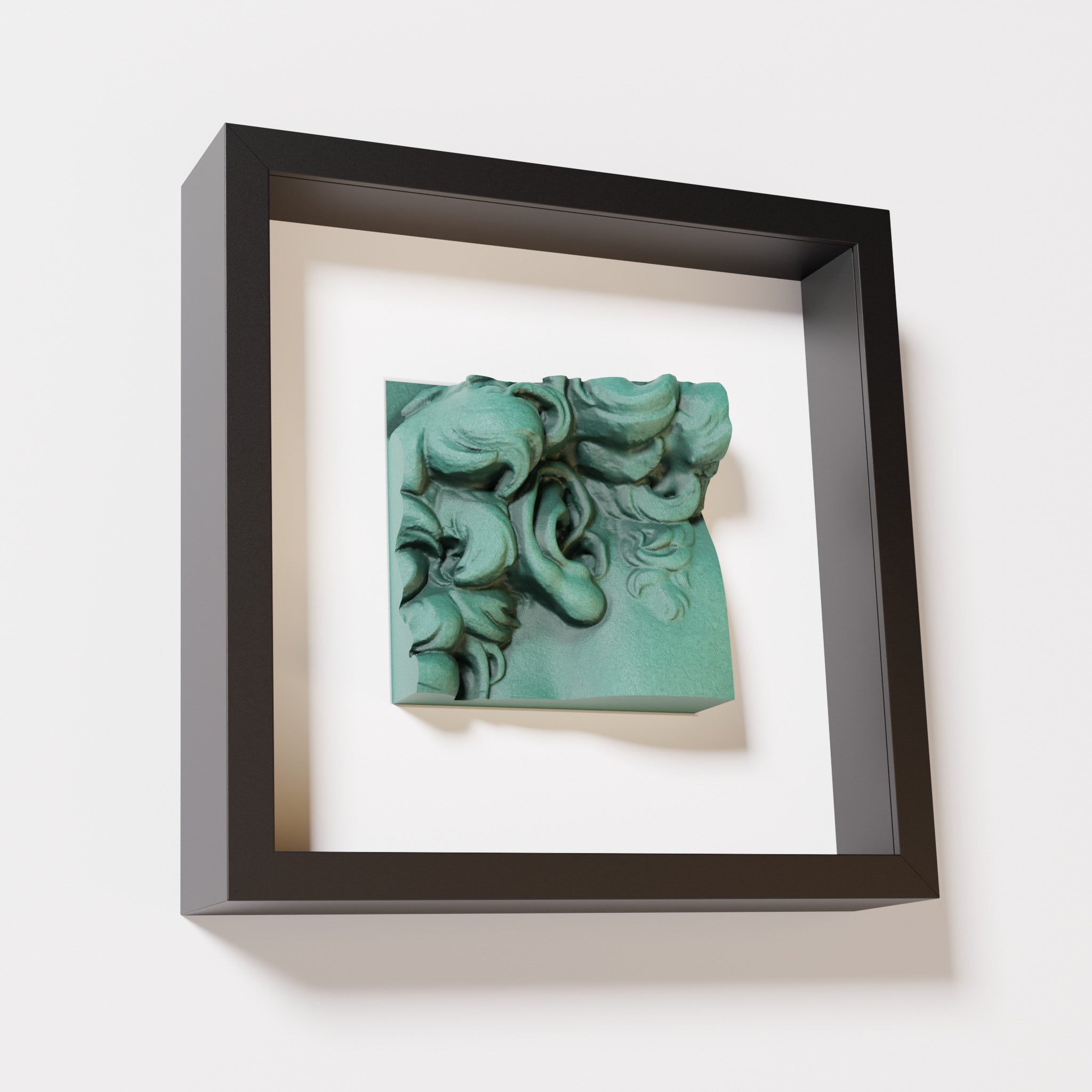 A close-up of a black shadowbox frame featuring an old patina sculpture of 'David's Ear.' The green textured finish and intricate curls stand out against the dark frame.