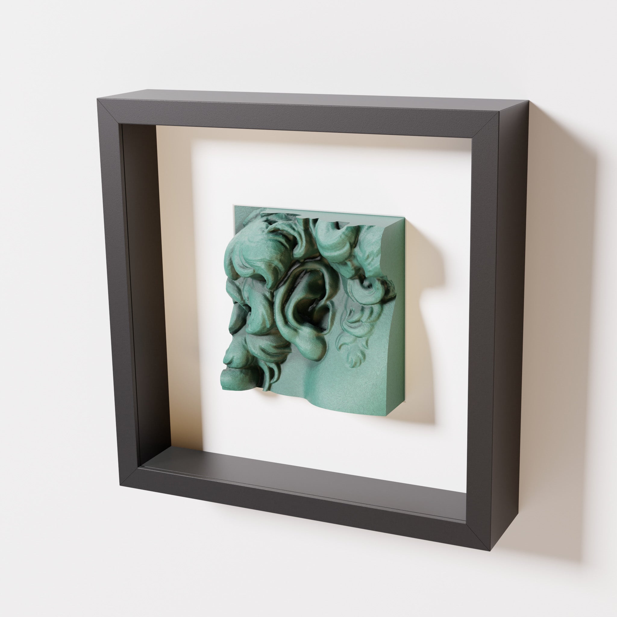 A close-up of a black shadowbox frame featuring an old patina sculpture of 'David's Ear.' The green textured finish and intricate curls stand out against the dark frame.