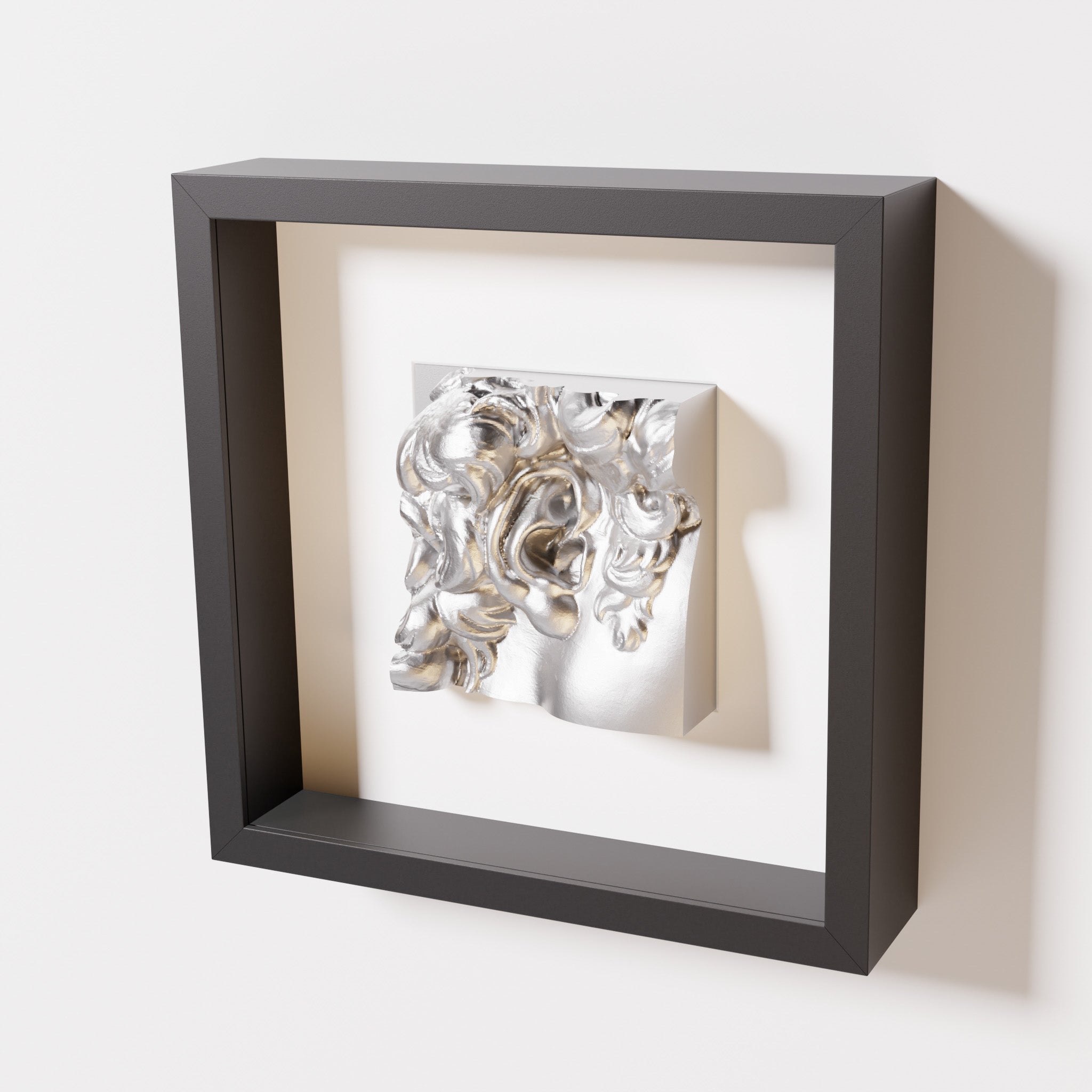 A close-up of a black shadowbox frame containing a chrome silver sculpture of 'David's Ear.' The shiny silver surface and intricate ear details contrast with the black frame.