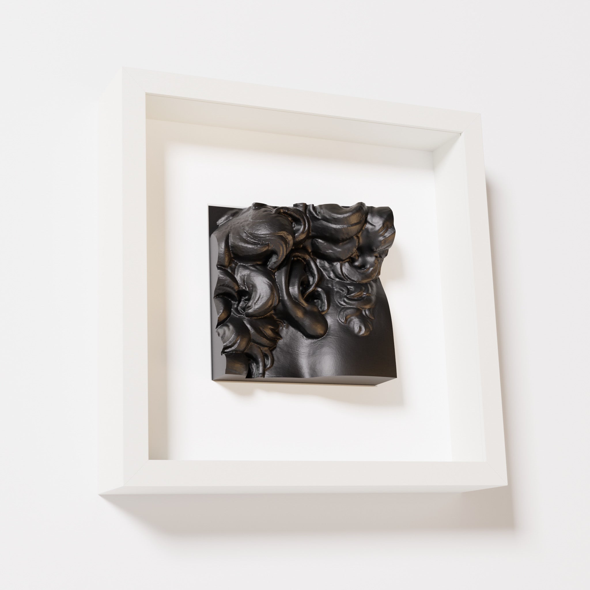 A close-up of a white shadowbox frame containing a matte black sculpture of 'David's Ear.' The artwork shows intricate curls and ear details, set against a minimalist white frame.