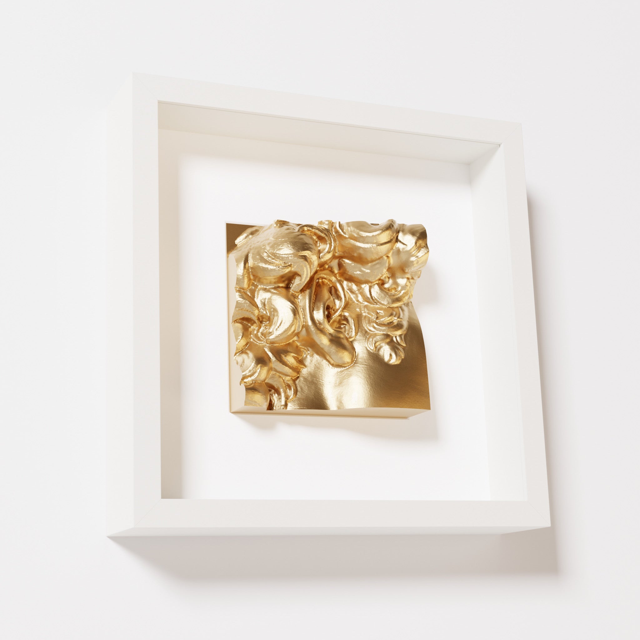 A close-up of a white shadowbox frame containing a chrome gold sculpture of 'David's Ear.' The reflective gold surface enhances the detailed curls and ear of the artwork.