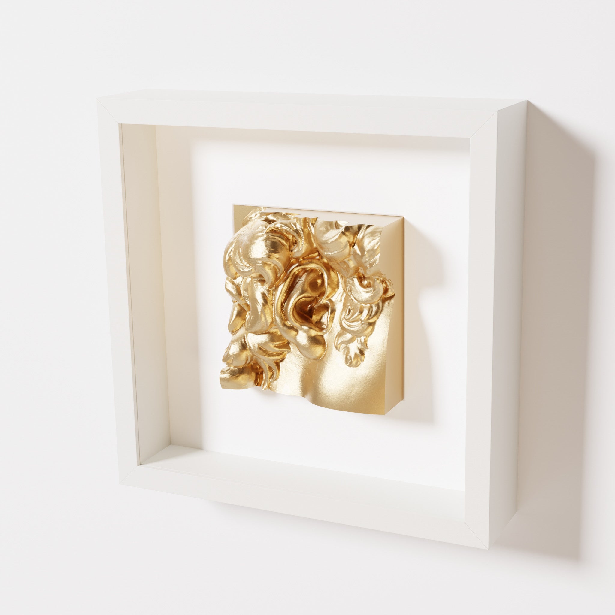 A close-up of a white shadowbox frame containing a chrome gold sculpture of 'David's Ear.' The reflective gold surface enhances the detailed curls and ear of the artwork.