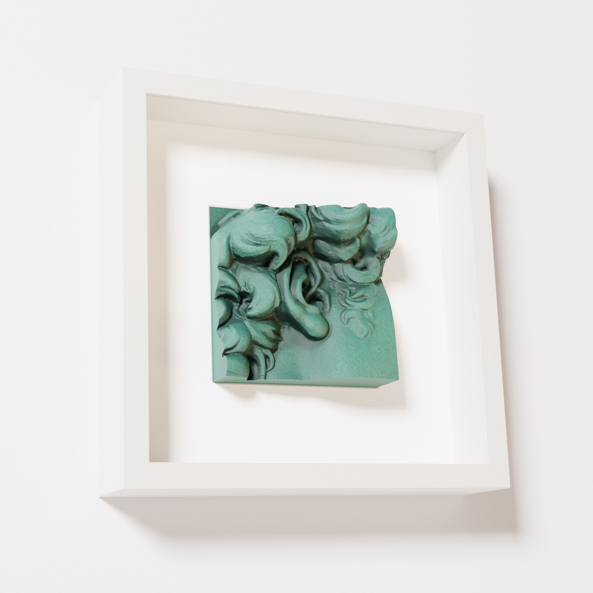 A close-up of a white shadowbox frame holding an old patina sculpture of 'David's Ear.' The green, weathered finish emphasizes the detailed curls and ear of the artwork.