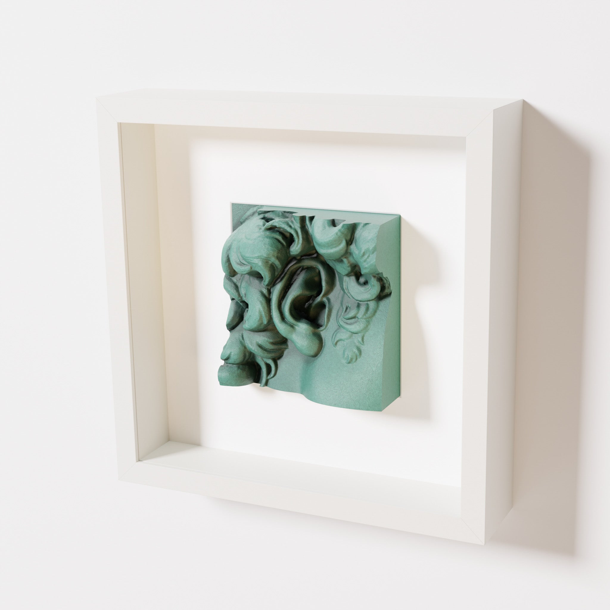 A close-up of a white shadowbox frame holding an old patina sculpture of 'David's Ear.' The green, weathered finish emphasizes the detailed curls and ear of the artwork.