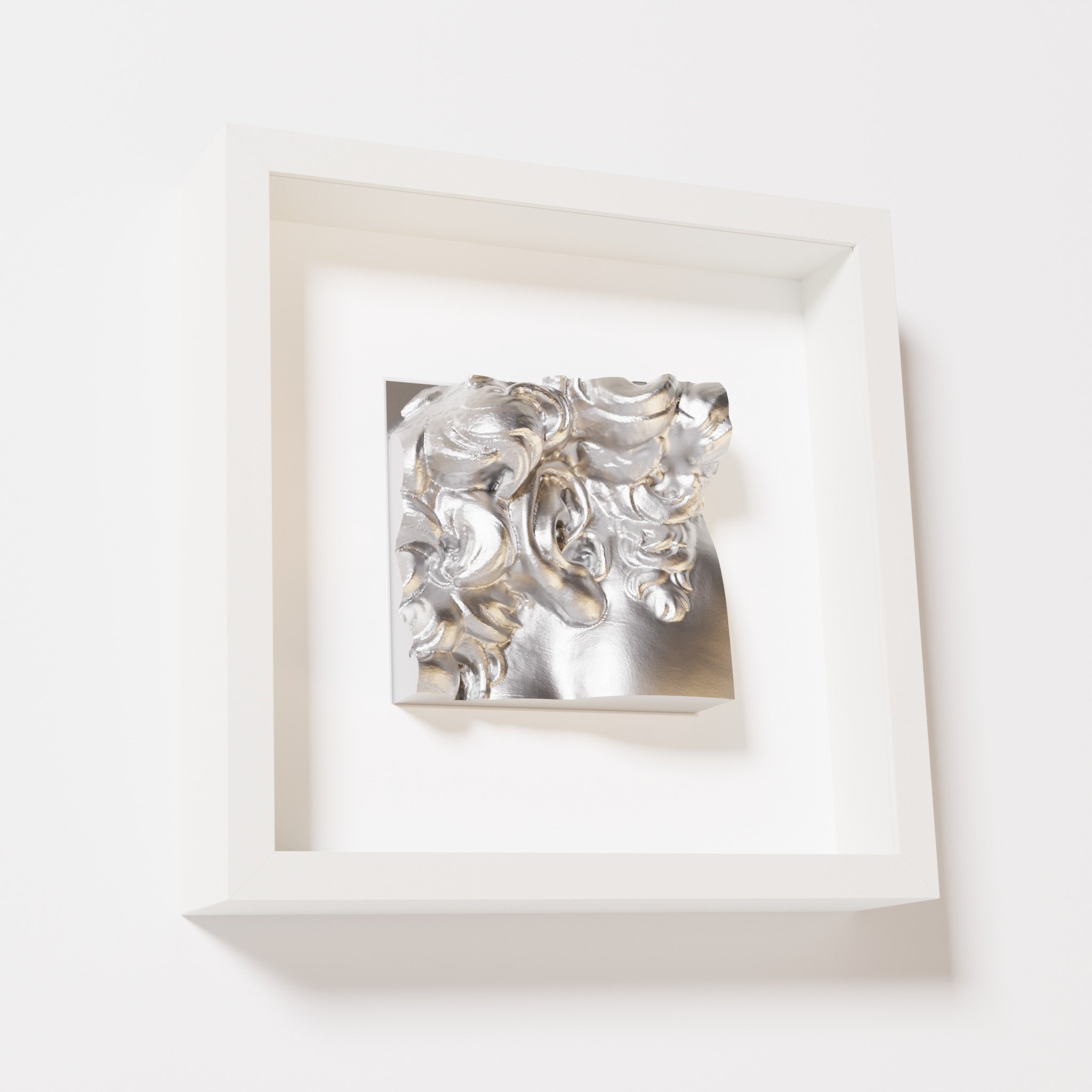 A close-up of a white shadowbox frame holding a chrome silver sculpture of 'David's Ear.' The reflective silver finish highlights the detailed curls and ear of the artwork.