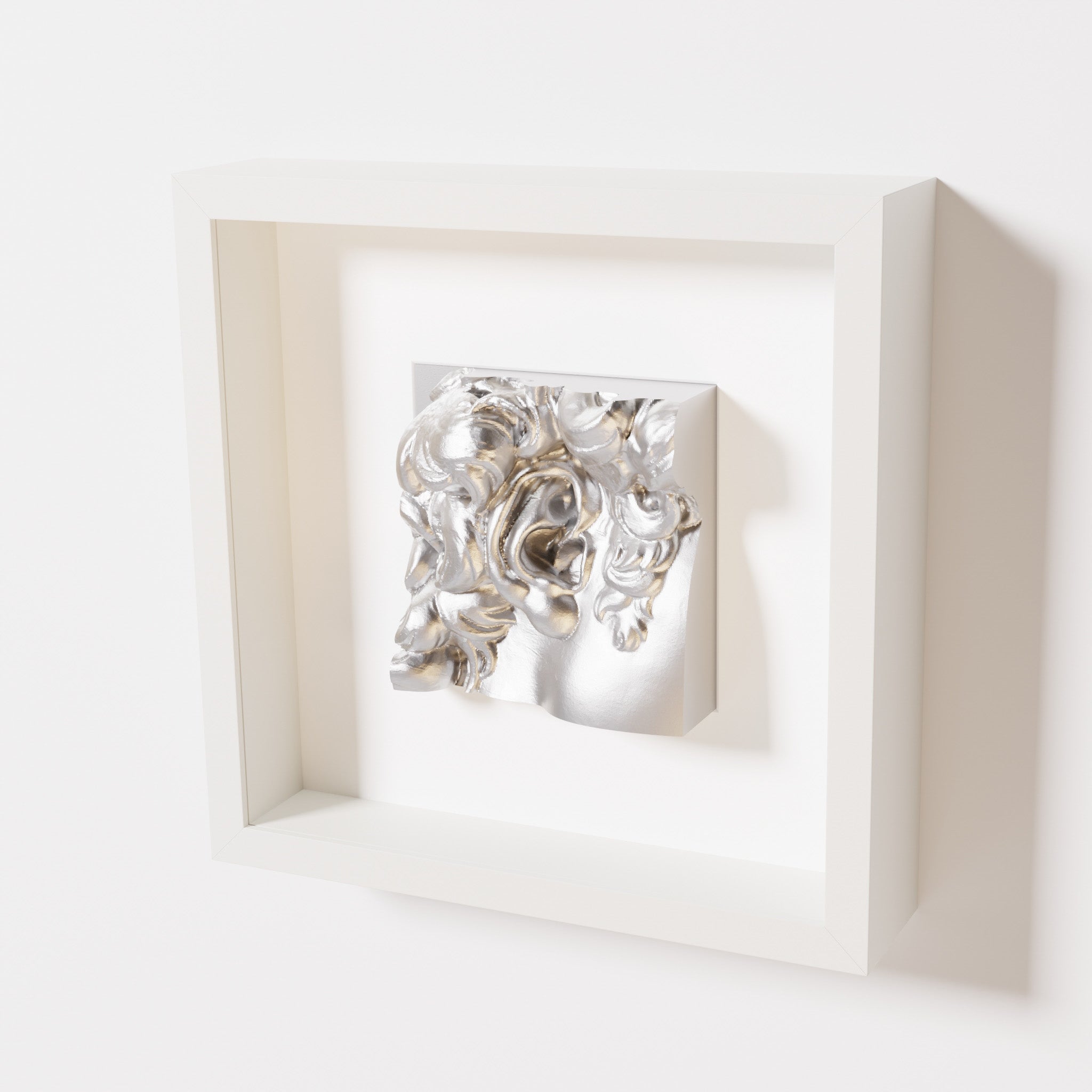 A close-up of a white shadowbox frame holding a chrome silver sculpture of 'David's Ear.' The reflective silver finish highlights the detailed curls and ear of the artwork.