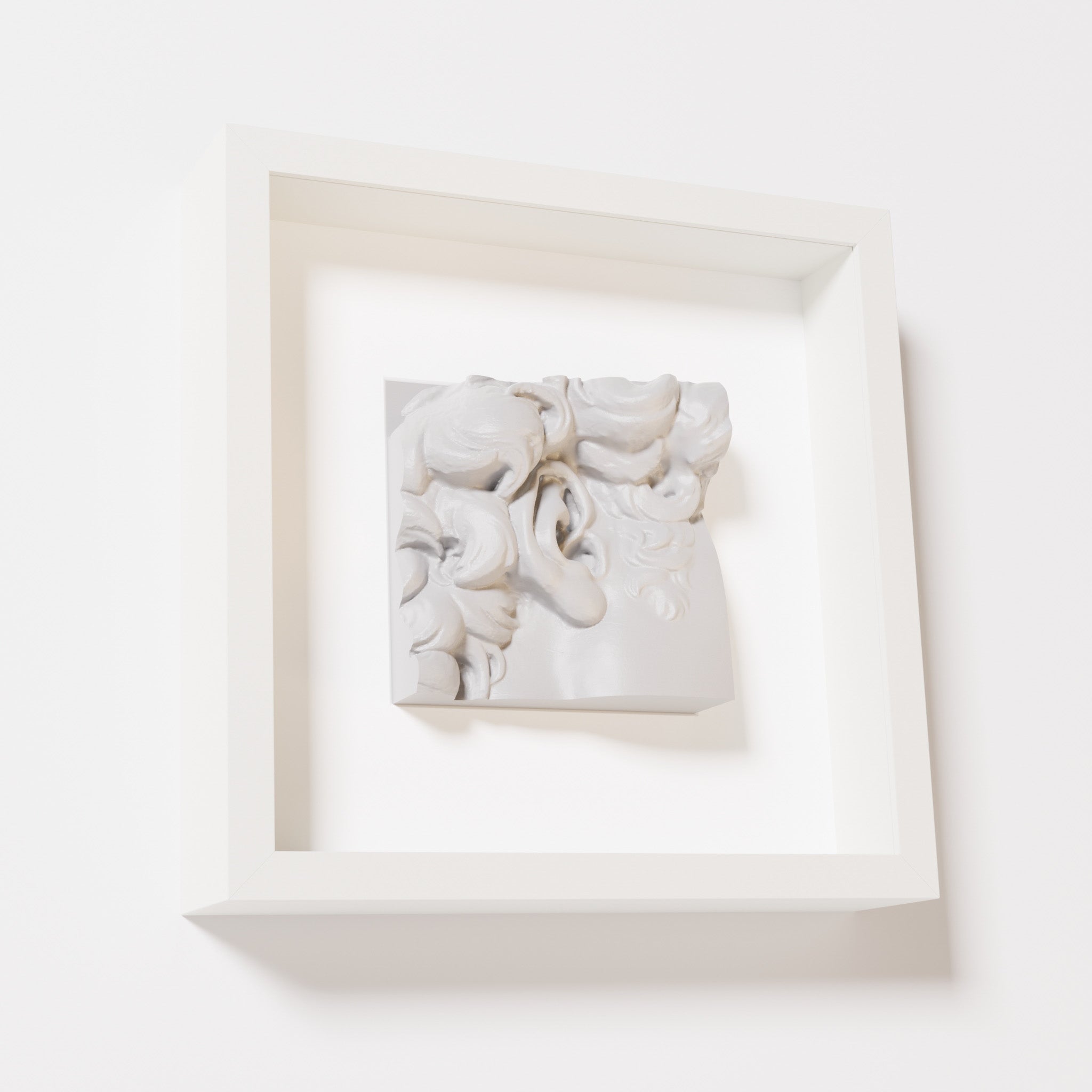 A close-up of a white shadowbox frame containing a marble white sculpture of 'David's Ear.' The intricate ear and curls are displayed with a smooth and clean aesthetic.