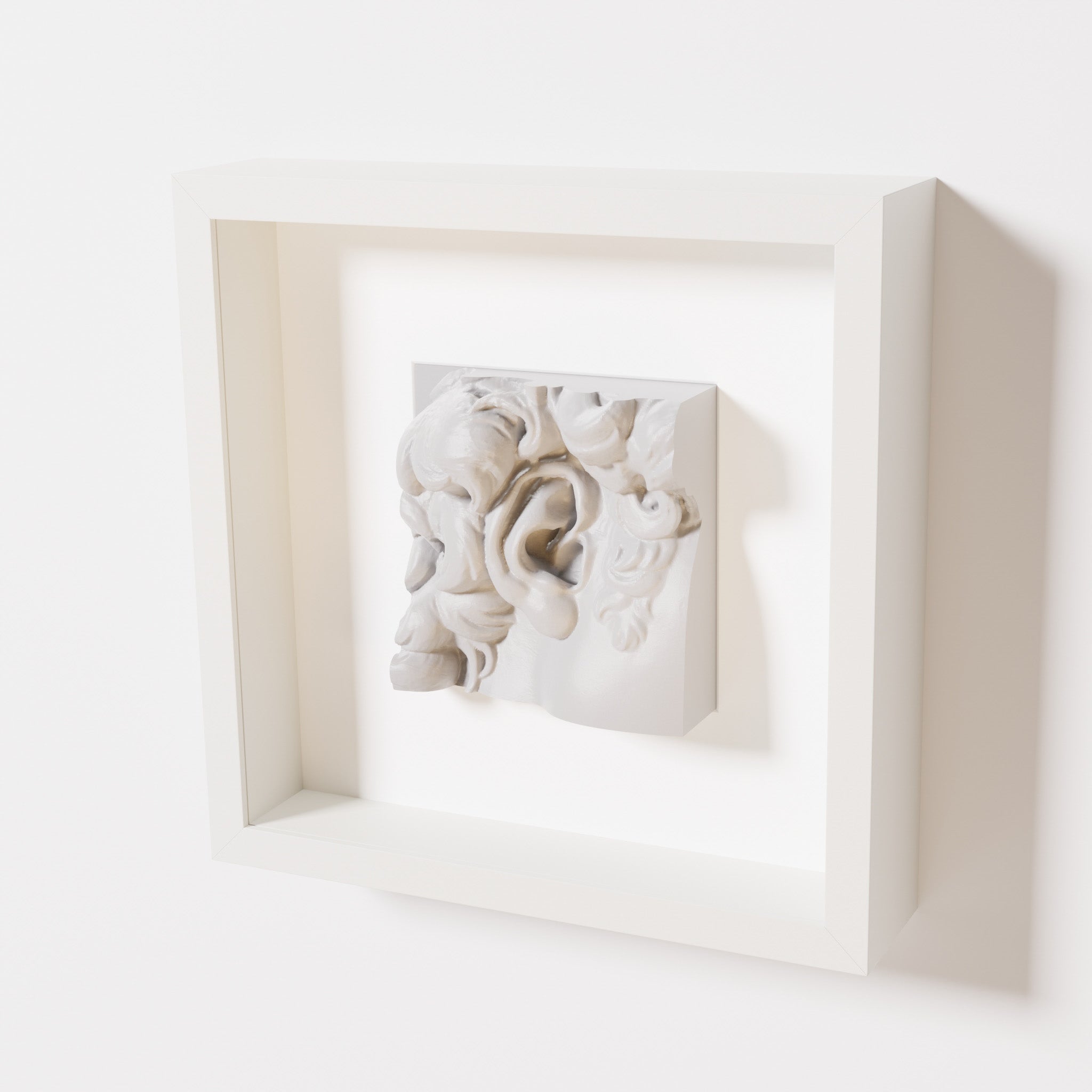 A close-up of a white shadowbox frame containing a marble white sculpture of 'David's Ear.' The intricate ear and curls are displayed with a smooth and clean aesthetic.