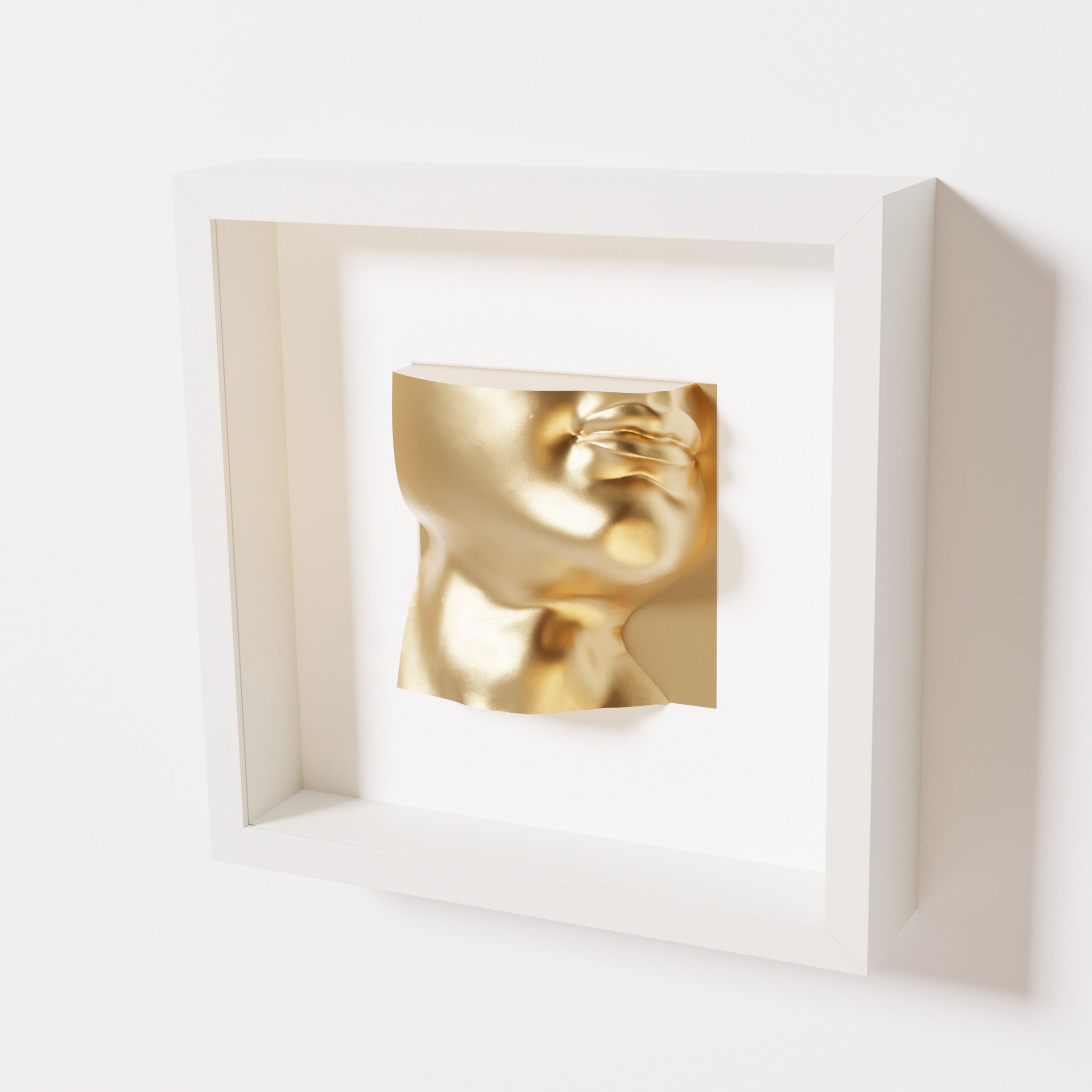 A close-up of a white shadowbox frame containing a chrome gold sculpture of 'David's Lip,' highlighting the detailed lips, chin, and reflective gold finish inspired by Michelangelo's David.