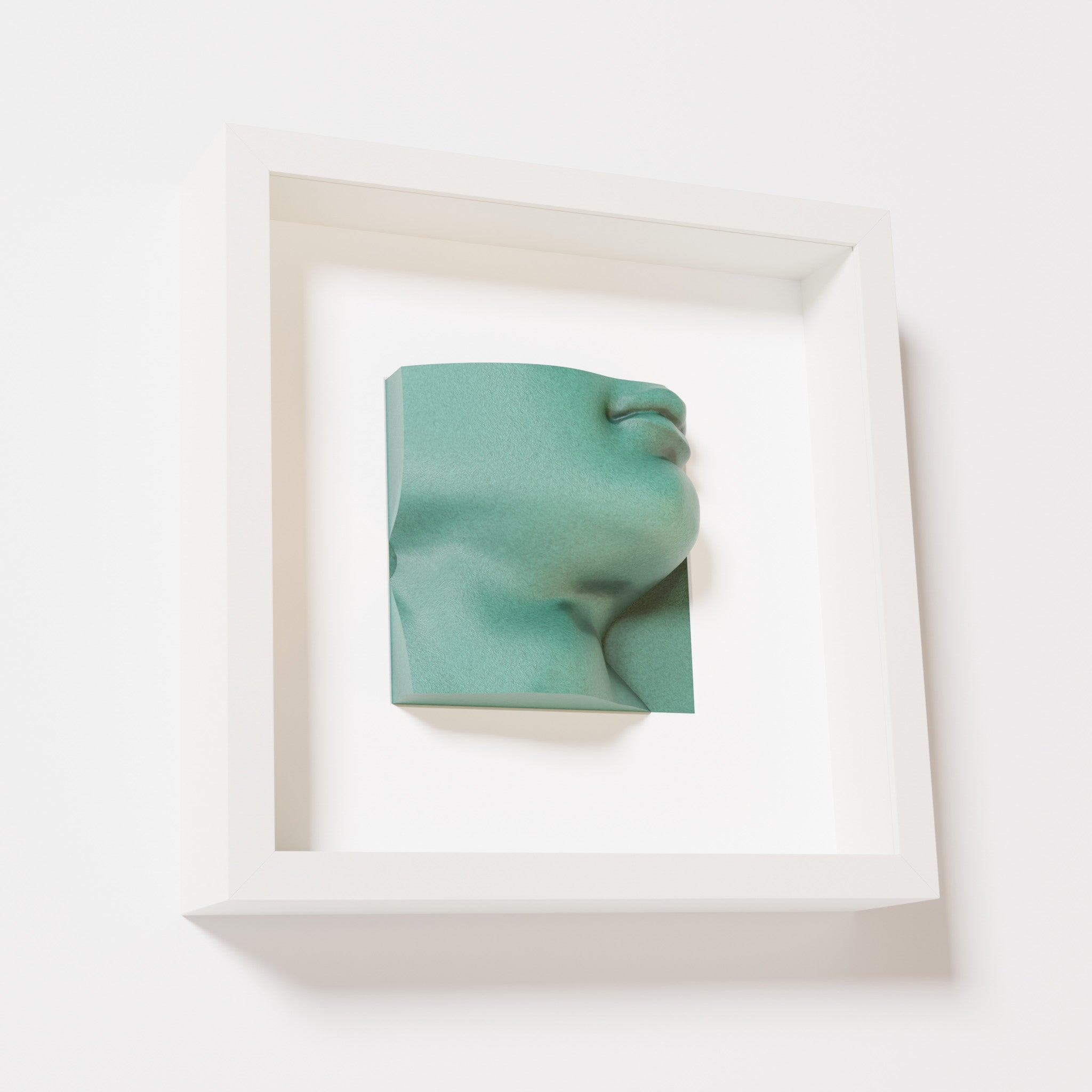 A close-up of a white shadowbox frame containing an old patina sculpture of 'David's Lip,' highlighting the detailed lips, chin, and textured green finish inspired by Michelangelo's David.