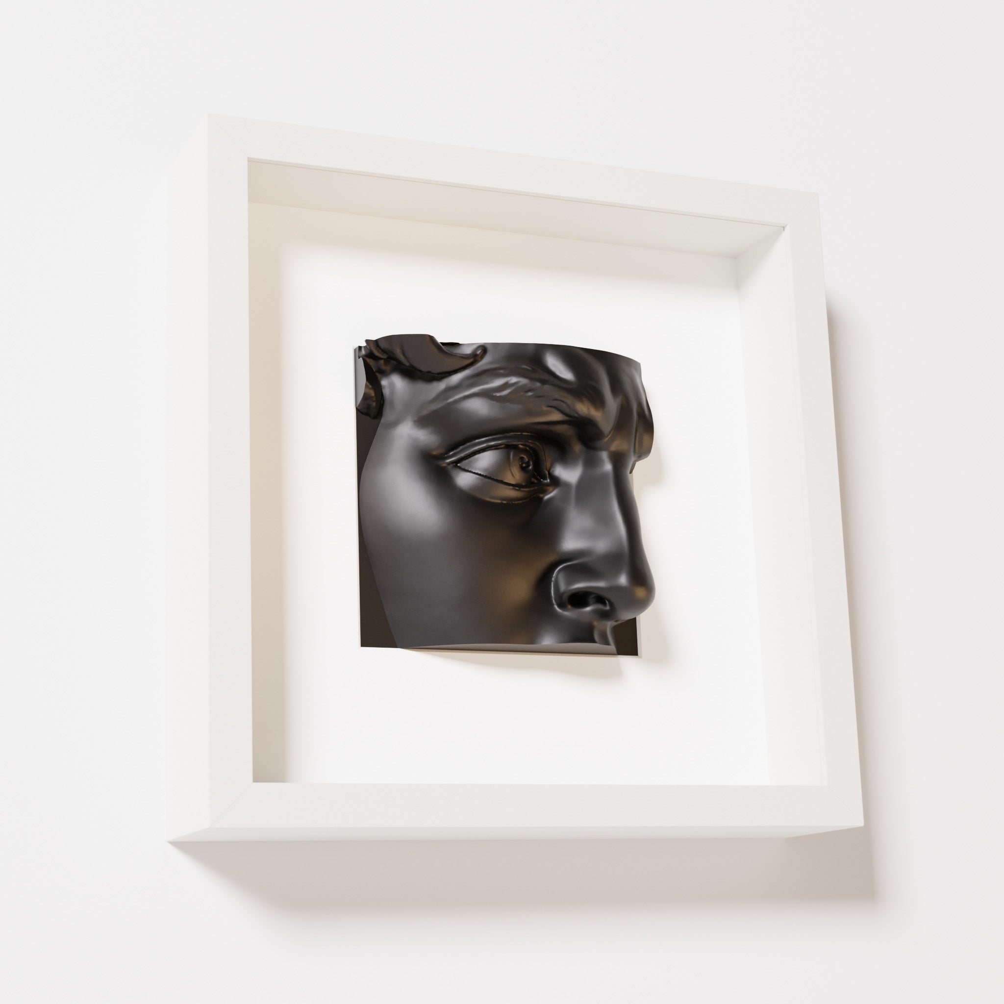 A close-up of a white shadowbox frame containing a matte black sculpture of 'David's Eye,' highlighting the intricate details of the eye, brow, and surrounding textures.