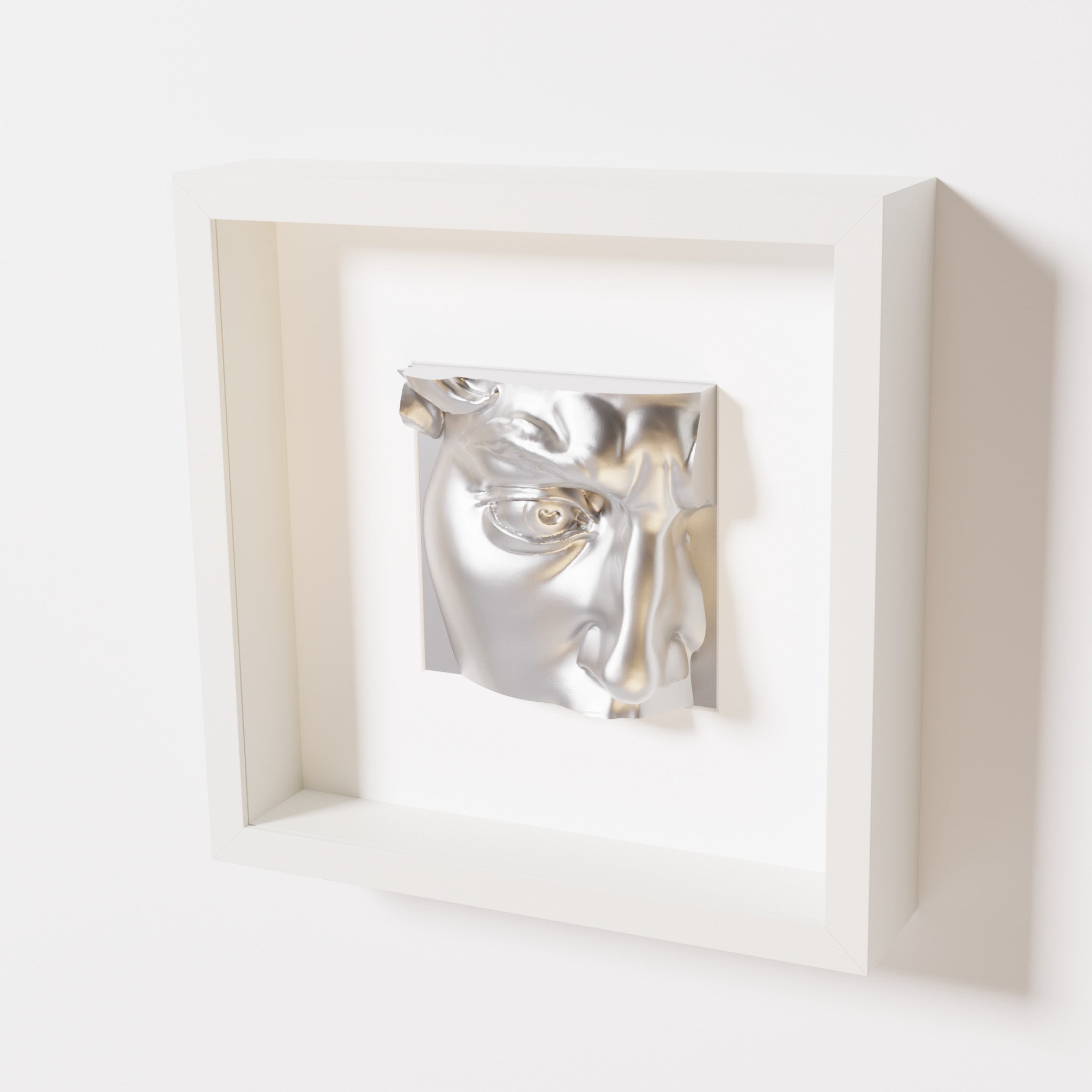 A close-up of a white shadowbox frame containing a chrome silver sculpture of 'David's Eye,' highlighting the intricate details of the eye, brow, and surrounding textures.