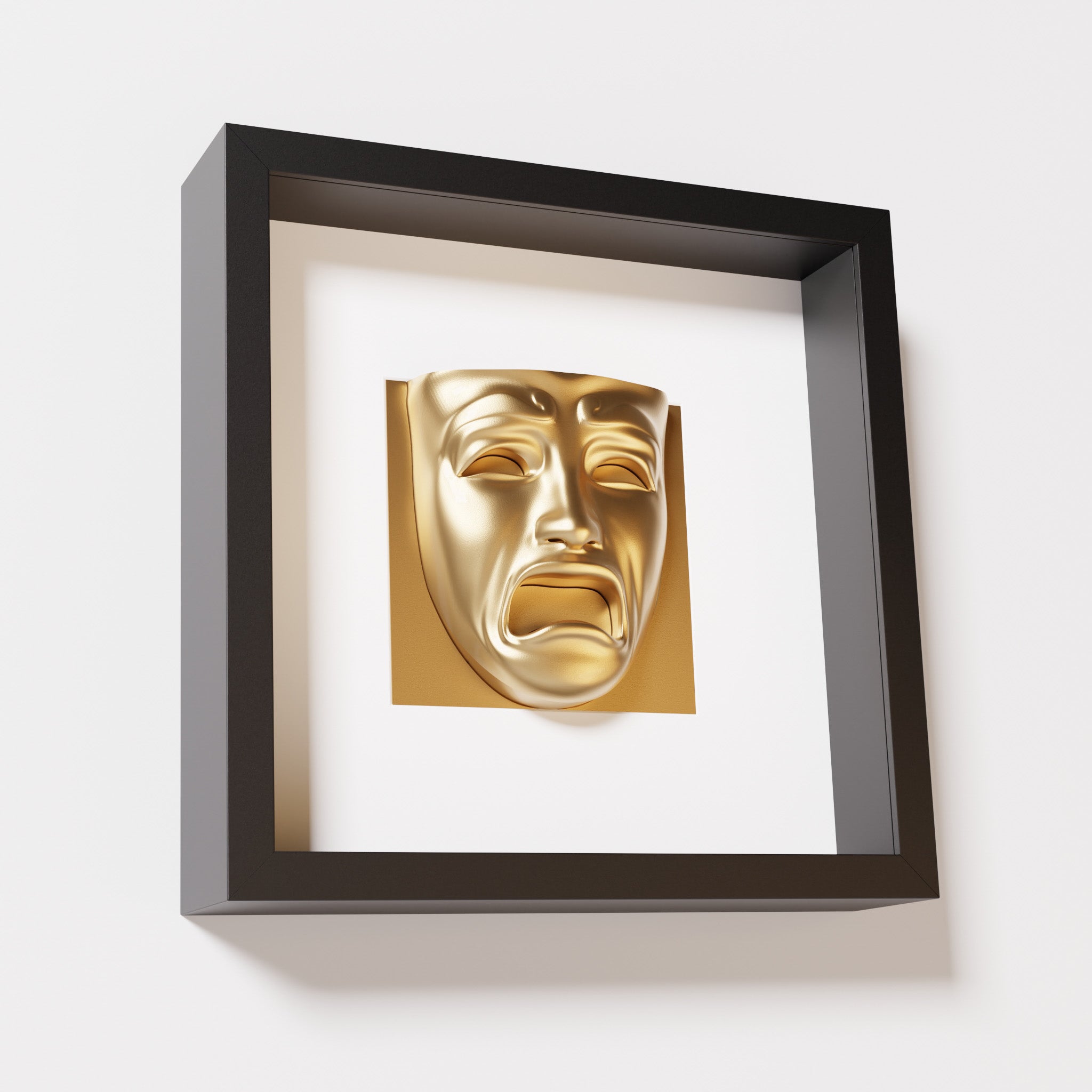 A close-up of a black shadowbox frame containing a chrome gold sculpture of 'Despair,' showcasing the expressive mask with furrowed brows, hollow eyes, and an open mouth.