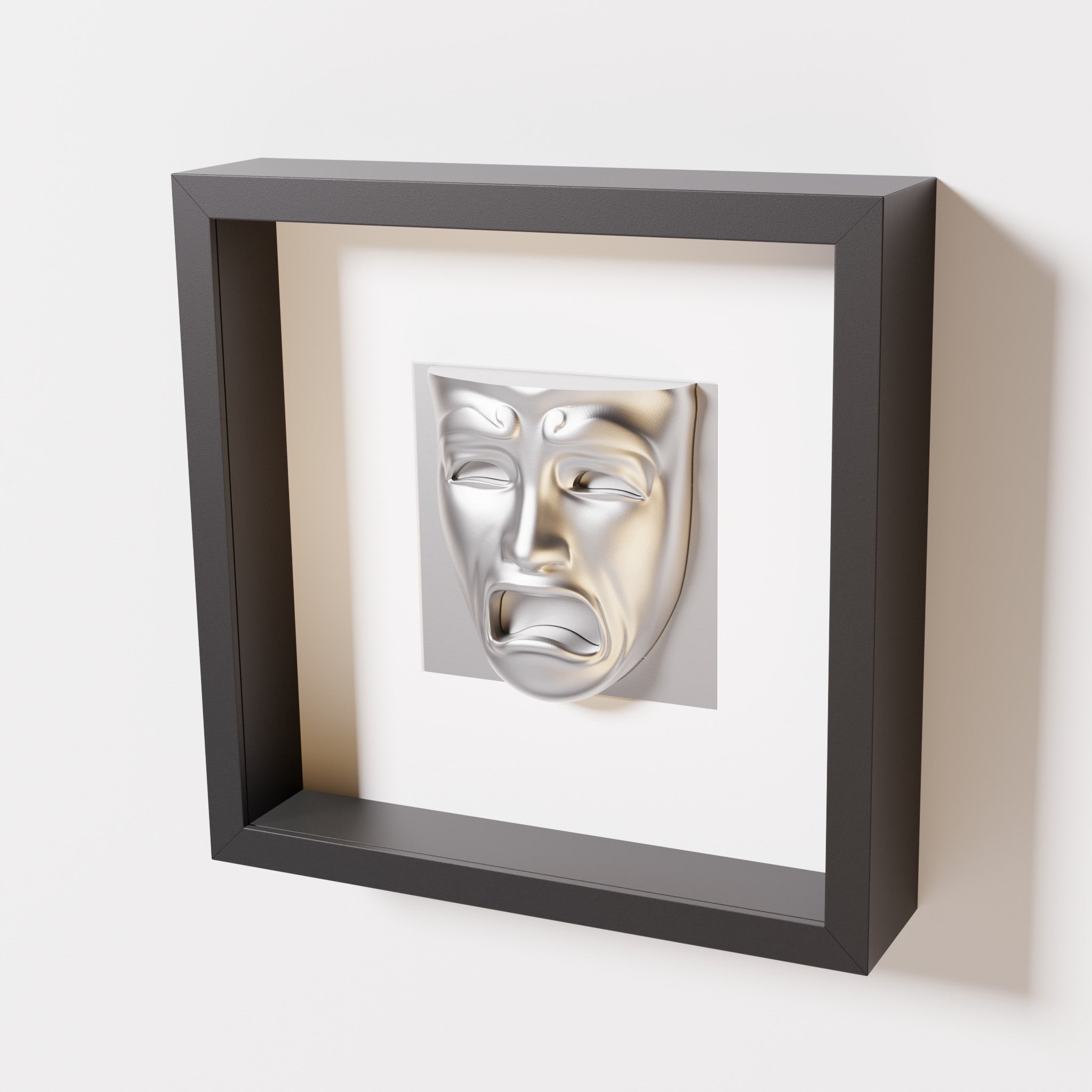 A close-up of a black shadowbox frame containing a chrome silver sculpture of 'Despair,' showcasing the expressive mask with furrowed brows, hollow eyes, and an open mouth.