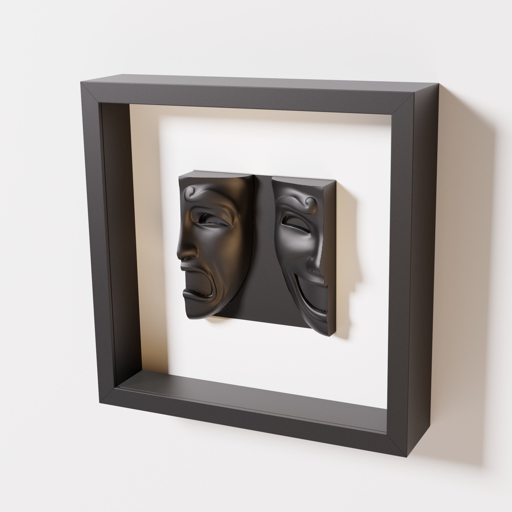 A close-up of a black shadowbox frame containing a matte black sculpture of 'Despair & Joy,' showcasing two expressive masks side by side: one with a sorrowful expression and the other with a joyful smile.