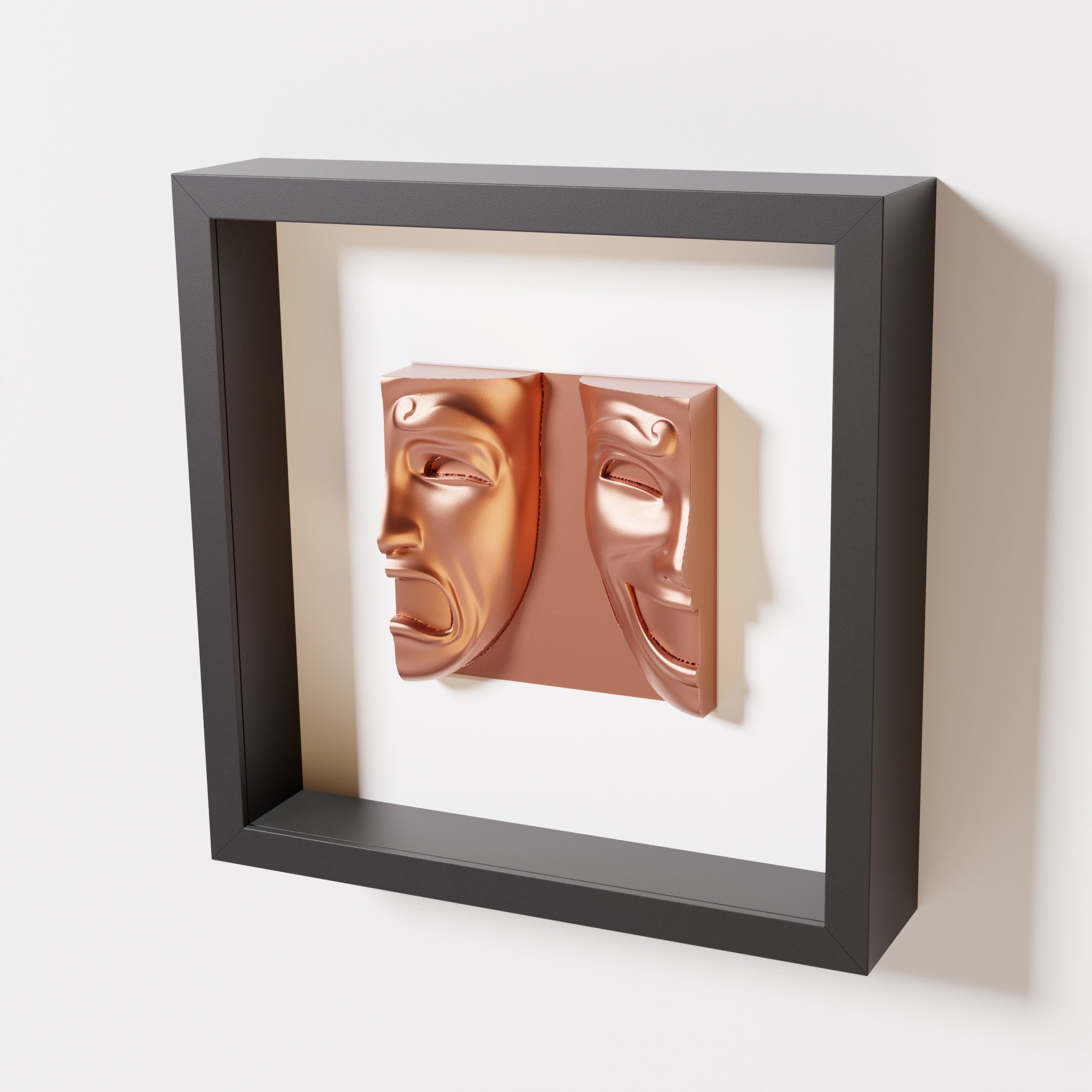 A close-up of a black shadowbox frame containing a chrome copper sculpture of 'Despair & Joy,' showcasing two expressive masks side by side: one with a sorrowful expression and the other with a joyful smile.