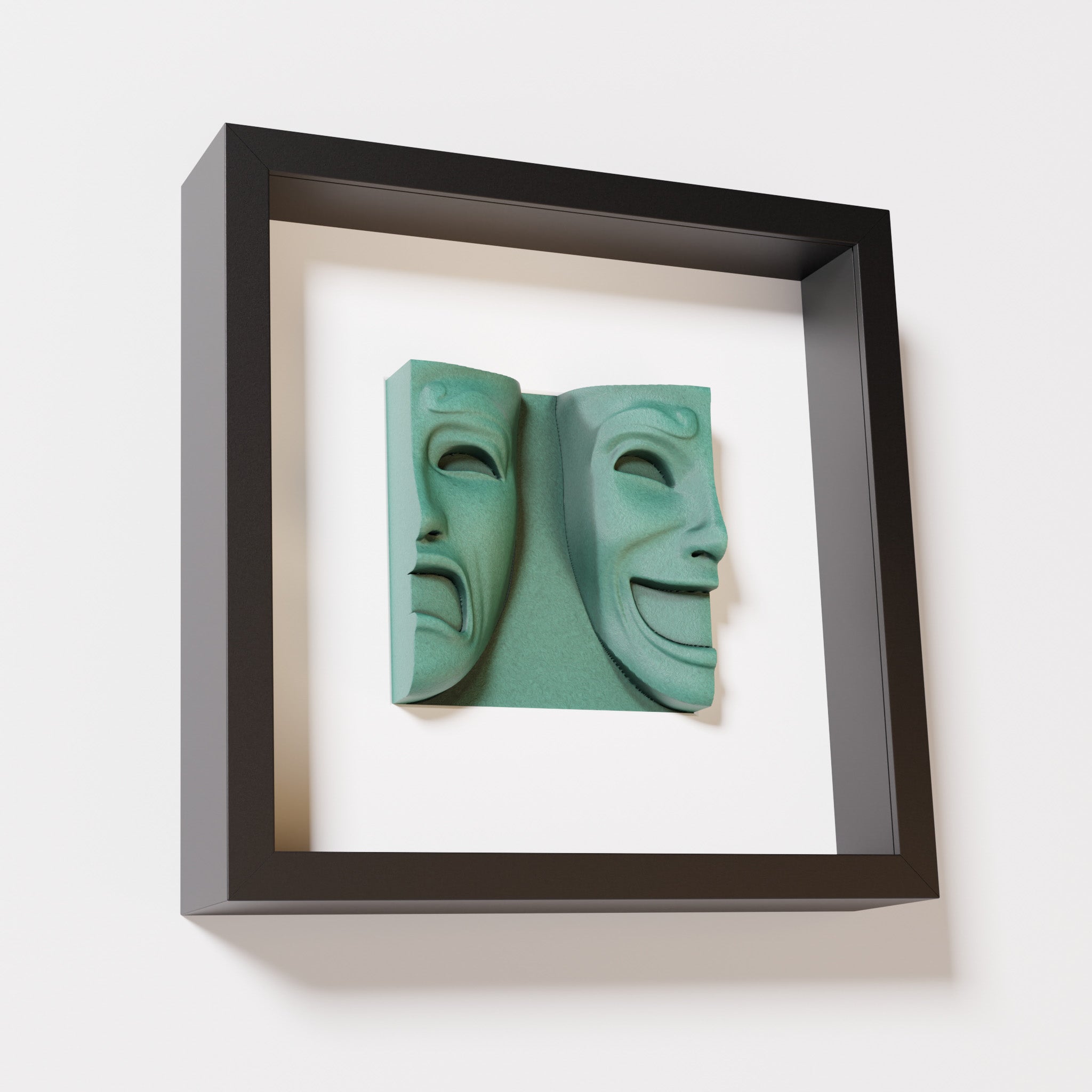 A close-up of a black shadowbox frame containing an old patina sculpture of 'Despair & Joy,' showcasing two expressive masks side by side: one with a sorrowful expression and the other with a joyful smile.