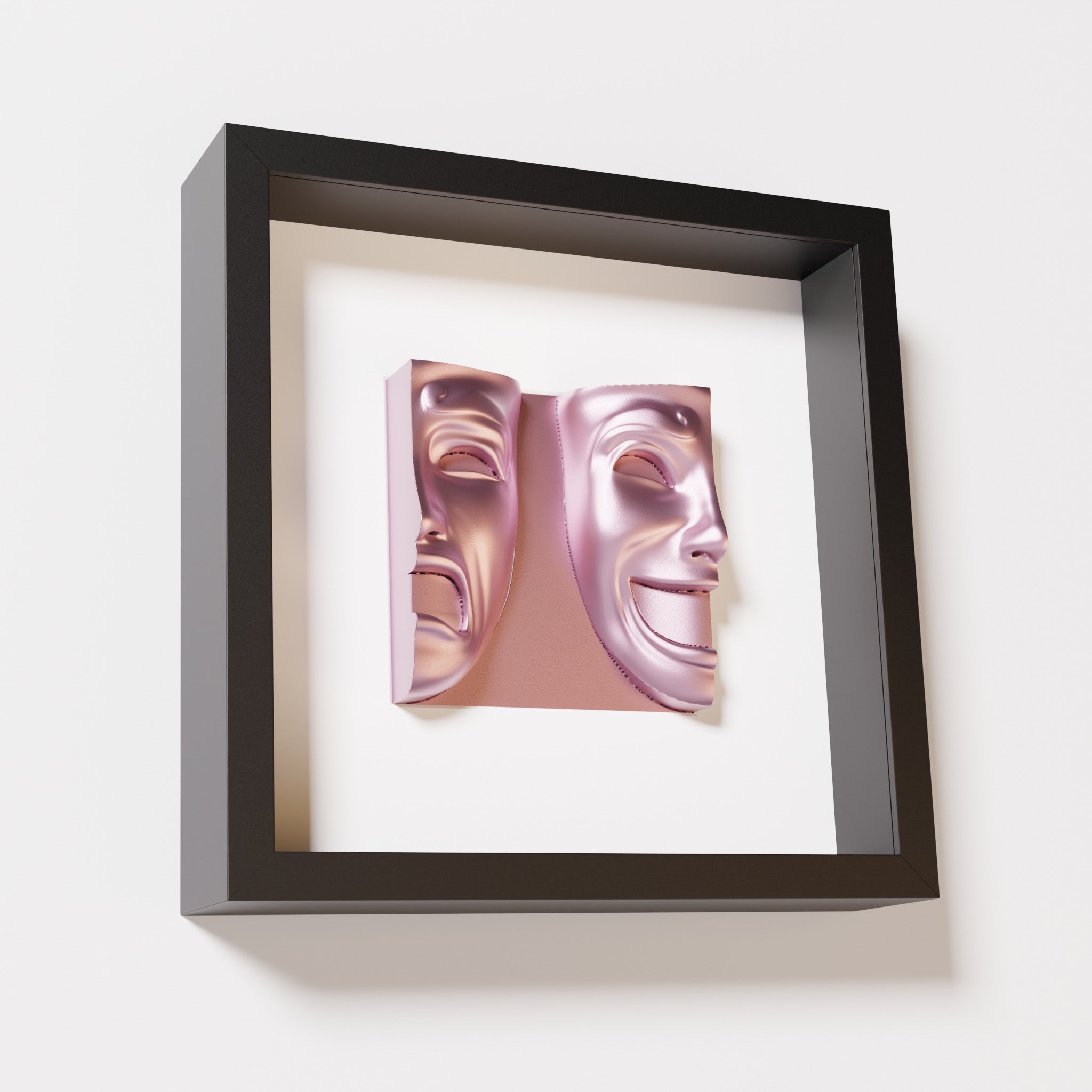 A close-up of a black shadowbox frame containing a metallic rose sculpture of 'Despair & Joy,' showcasing two expressive masks side by side: one with a sorrowful expression and the other with a joyful smile.