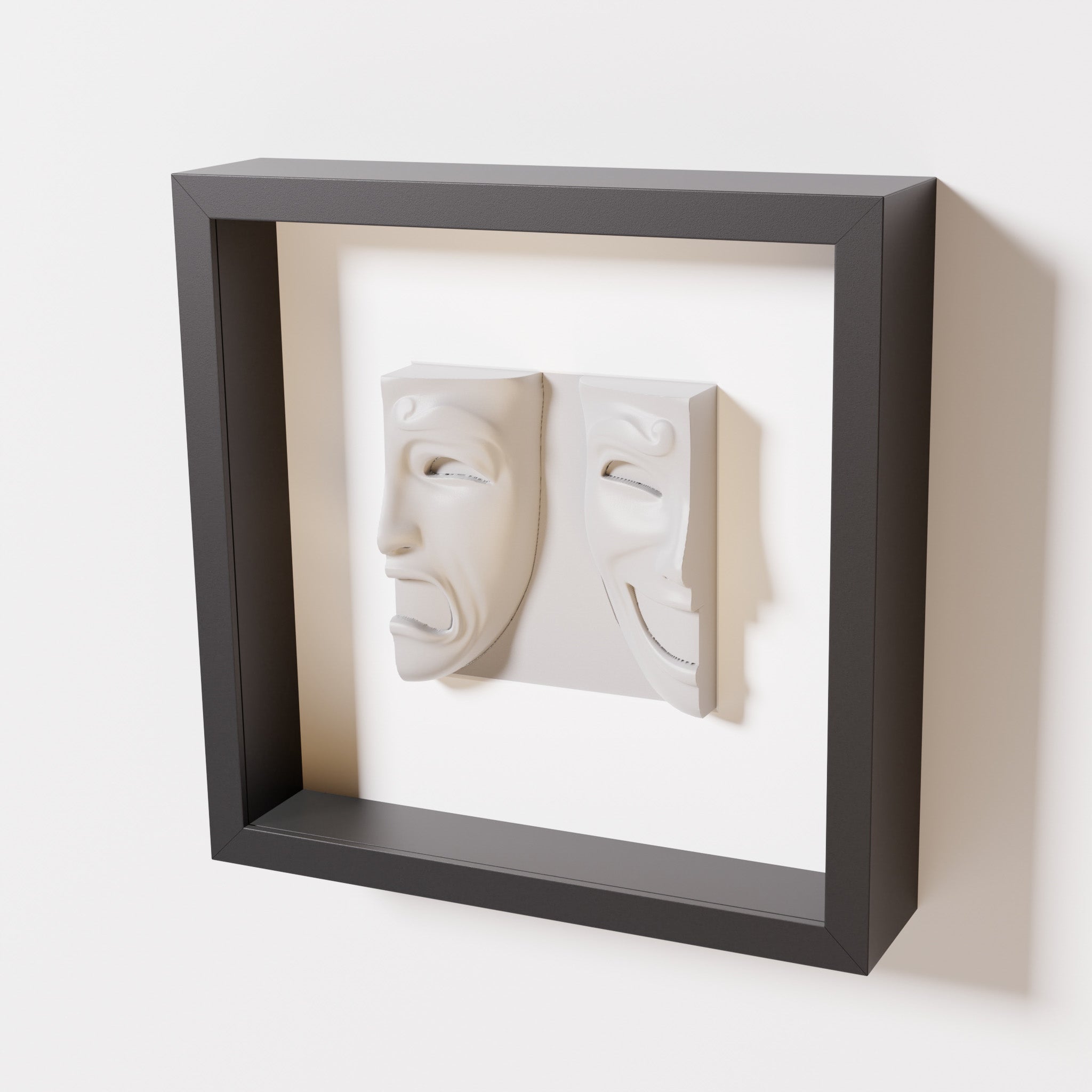 A close-up of a black shadowbox frame containing a marble white sculpture of 'Despair & Joy,' showcasing two expressive masks side by side: one with a sorrowful expression and the other with a joyful smile.